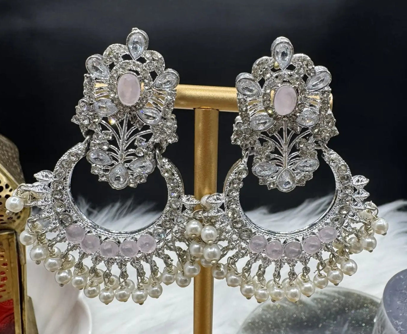 Pakistani style traditional silver earrings with pearls and pink gemstones on a stand against a dark background