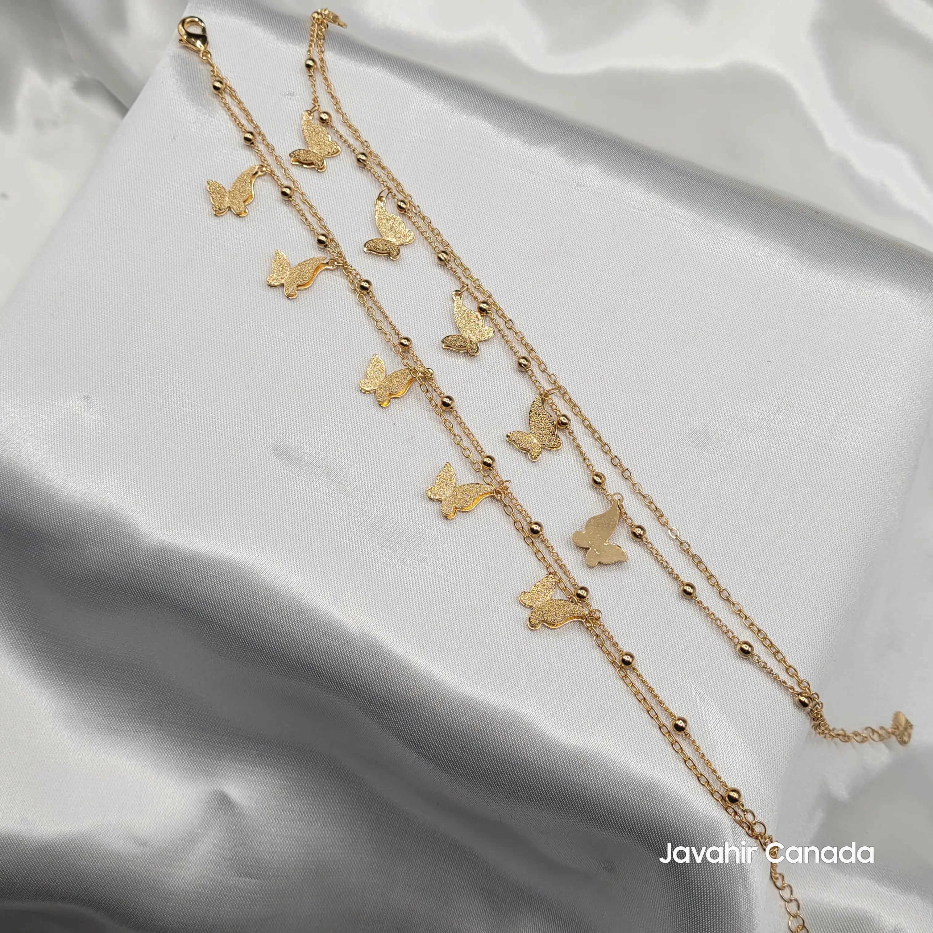 Set of 2 butterfly anklets in gold tone displayed on satin background