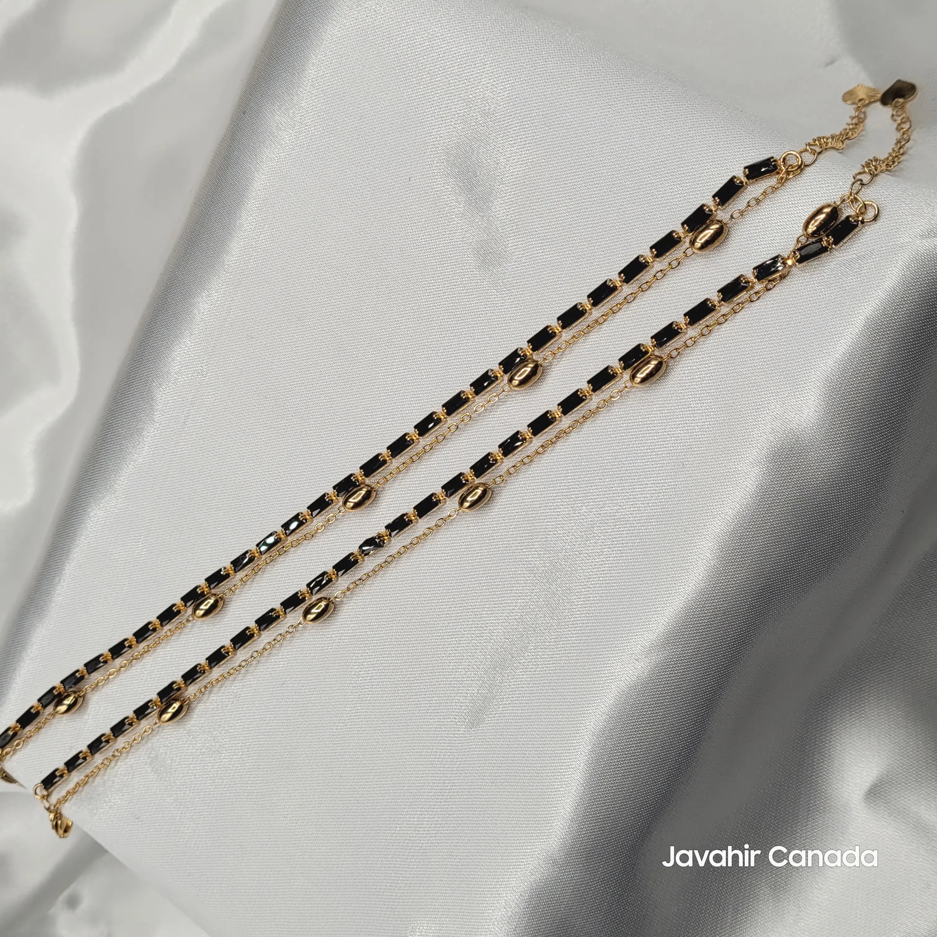 JV5007 gold plated anklet pair with rectangular black stones and gold beads on satin background