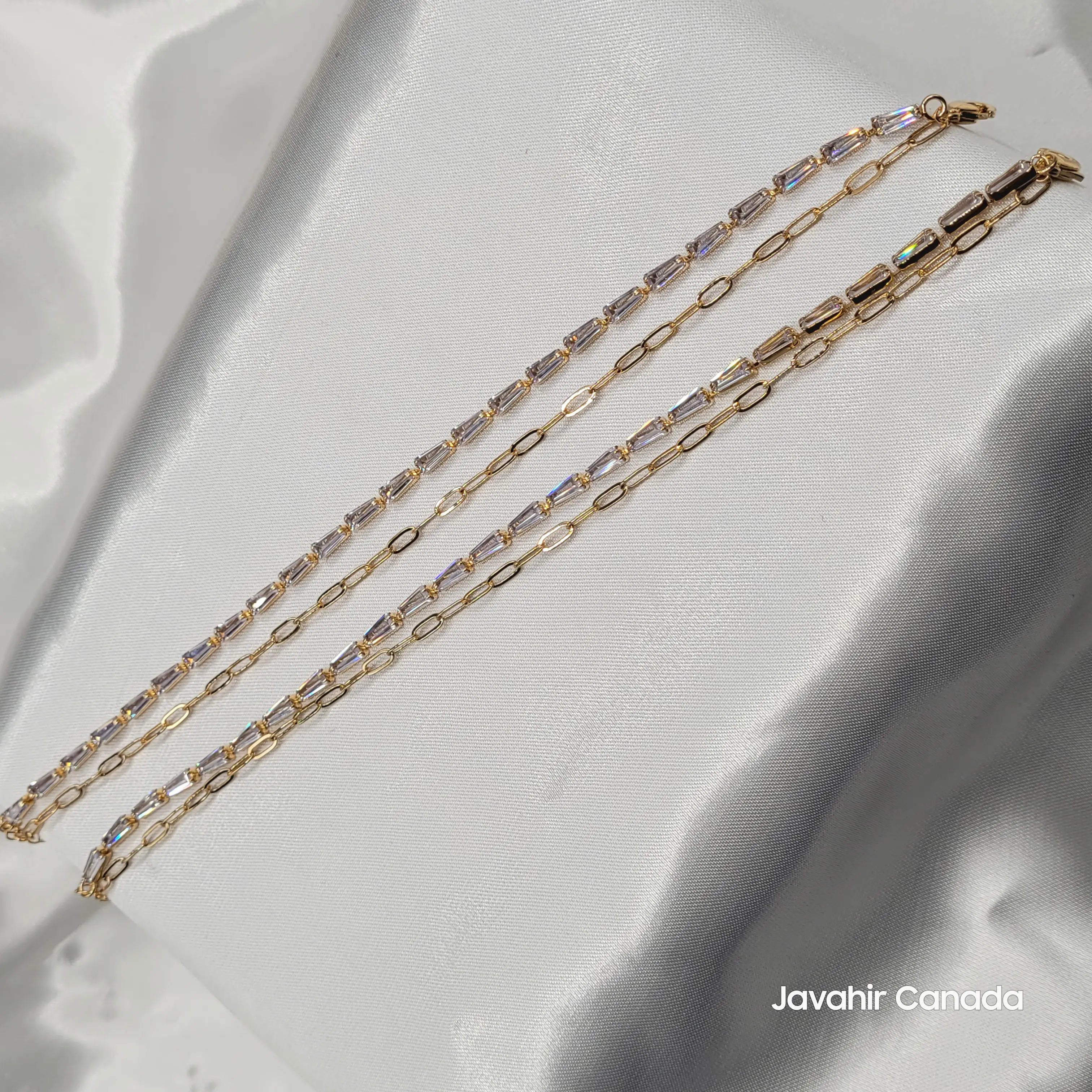 JV5008 gold plated anklet pair with clear baguette-cut stones and chain links on satin background