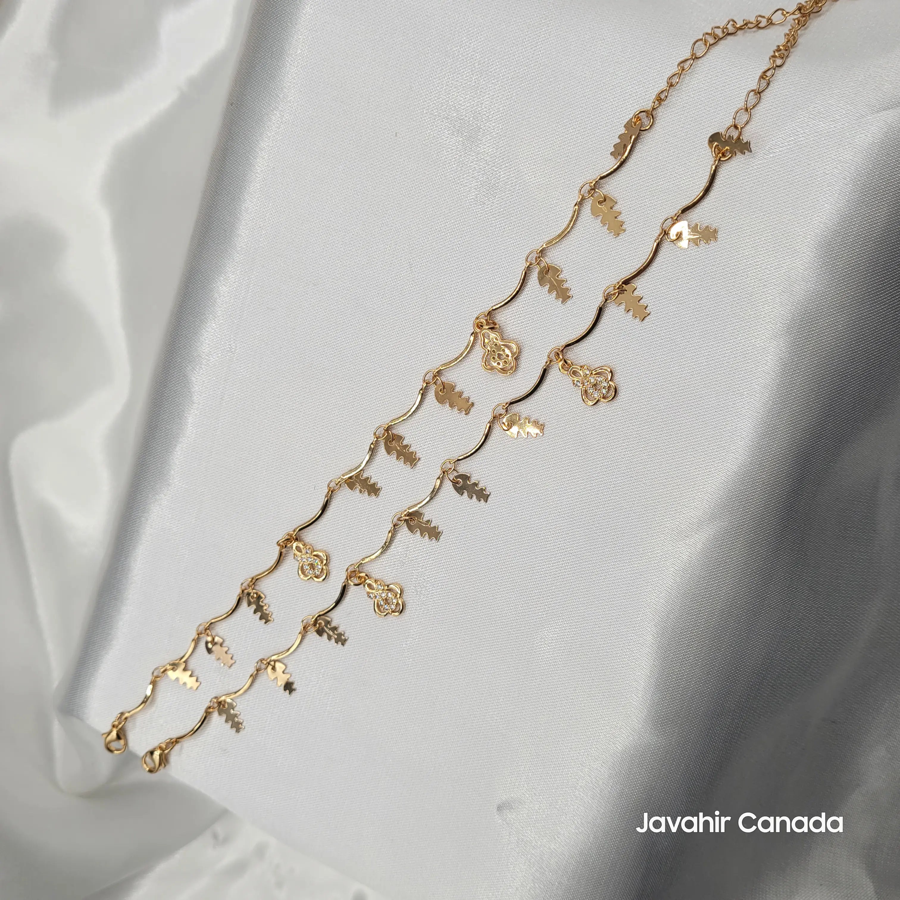 JV5015 gold-plated anklet pair with leaf and floral charms on wavy chain, displayed on white satin