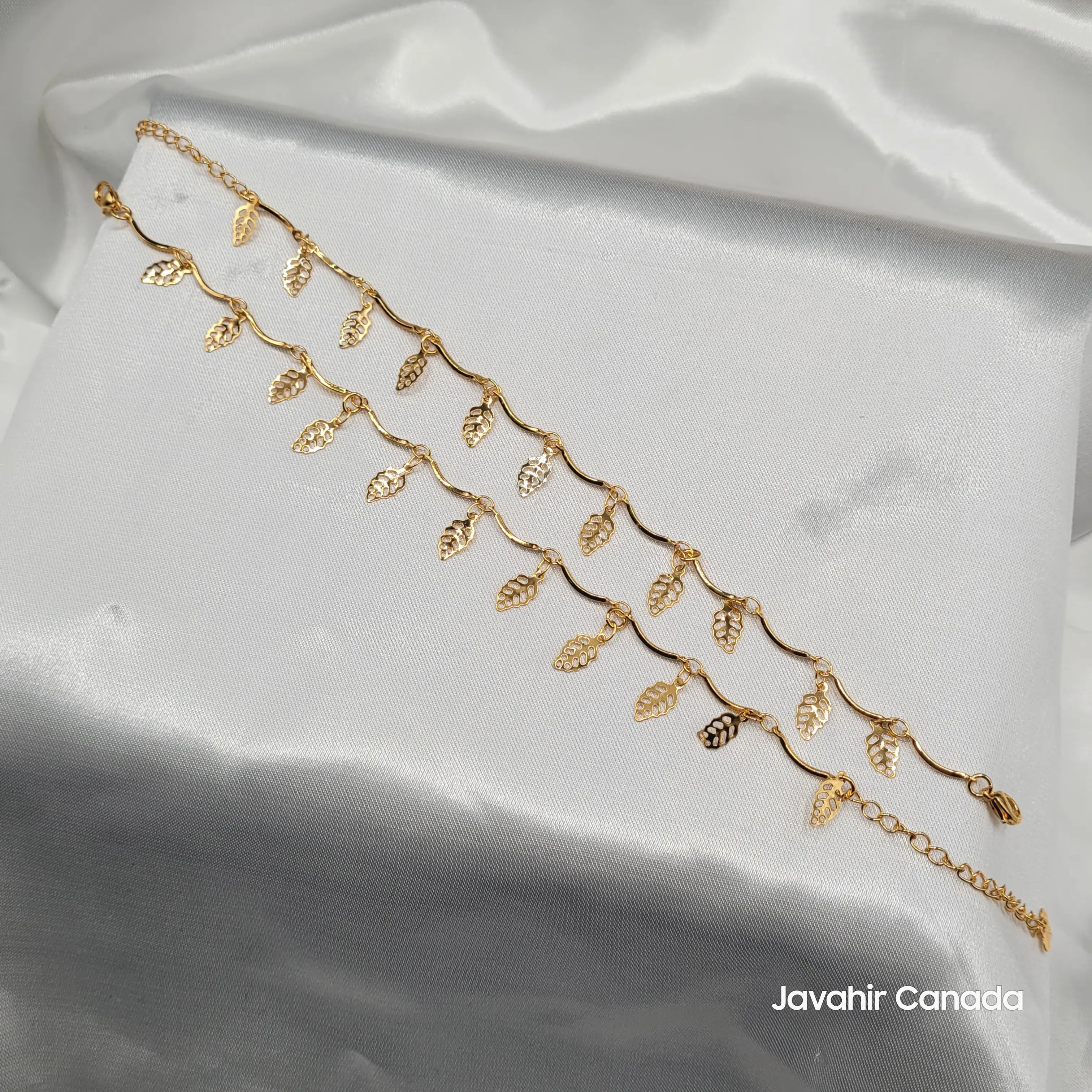 JV5021 gold anklet with wavy chain and hanging leaf charms displayed on satin fabric