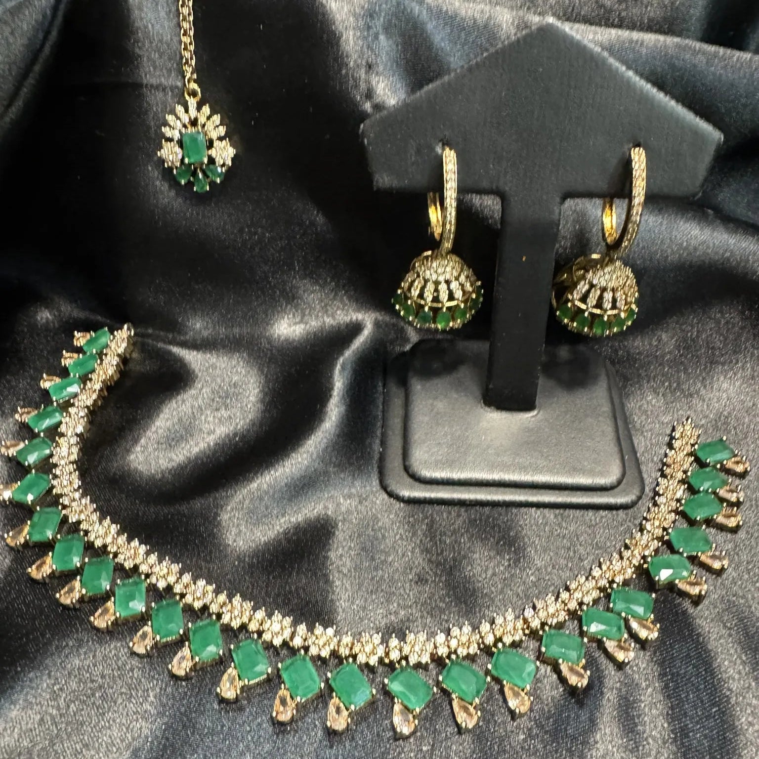 Green and gold jewelry set including necklace, earrings, and teeka on a black satin background