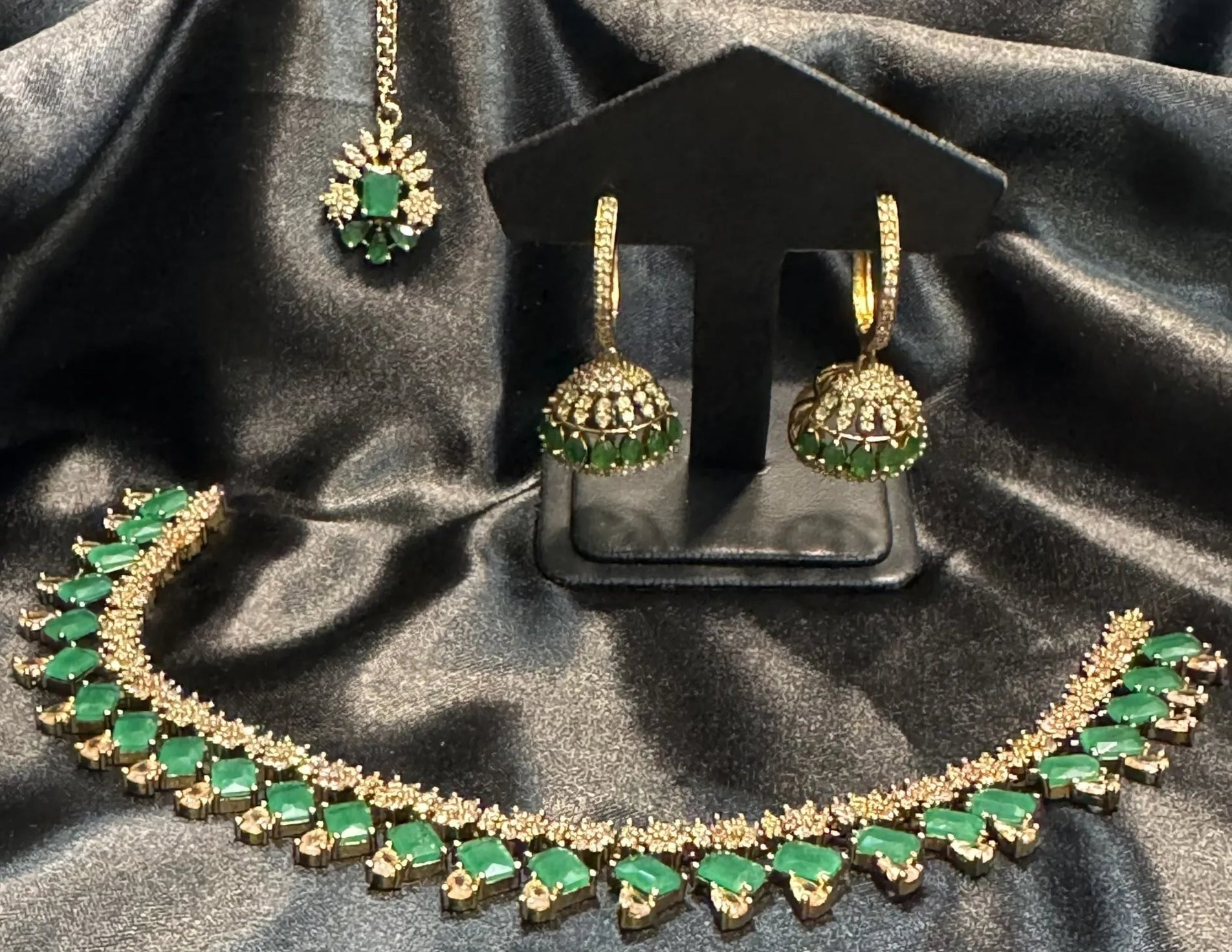 Jewelry set with necklace, earrings, and teeka on a black satin background