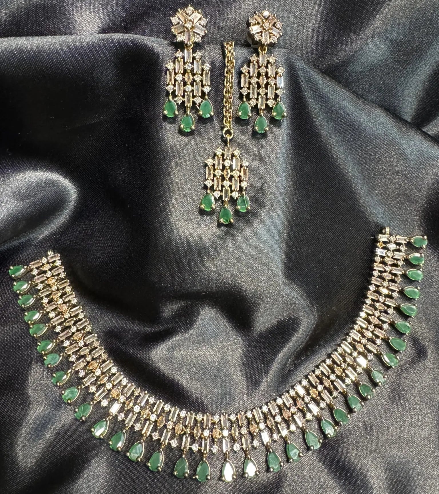 gold plated necklace set with green stones and black background