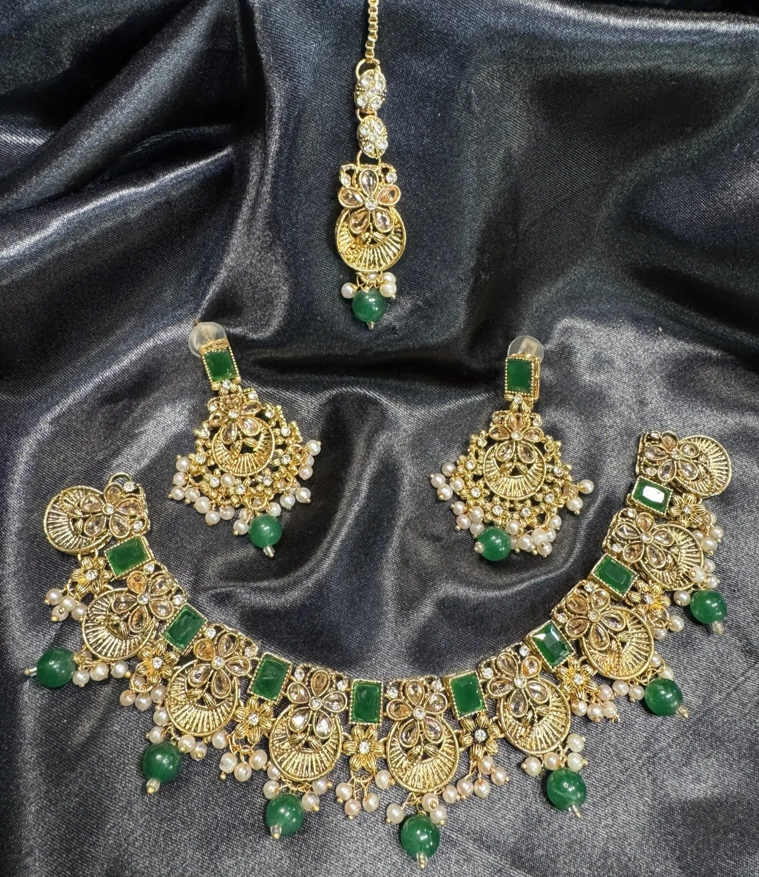 Gold and green jewelry set on a dark fabric background