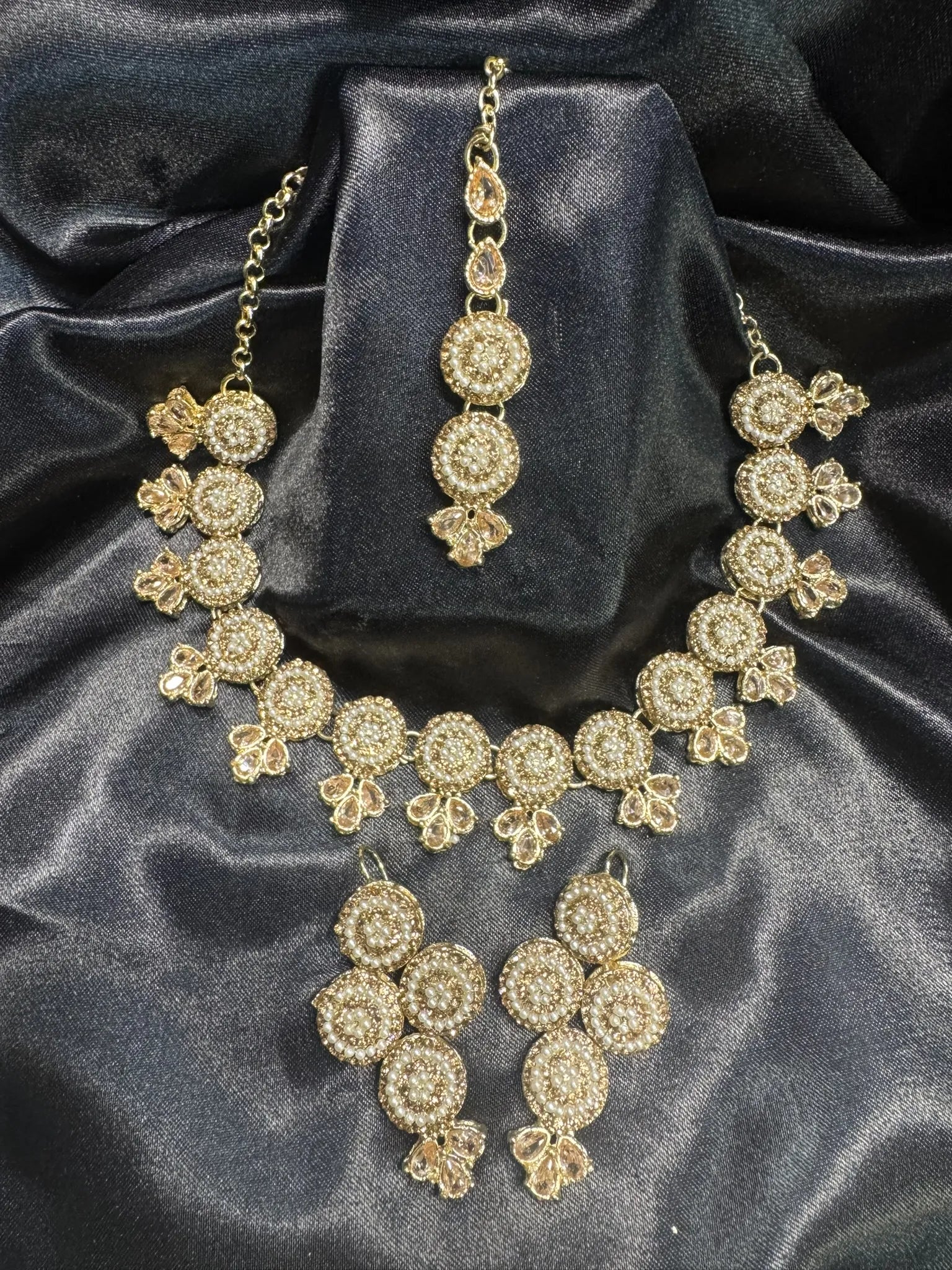 Gold necklace and earrings set on a dark satin background