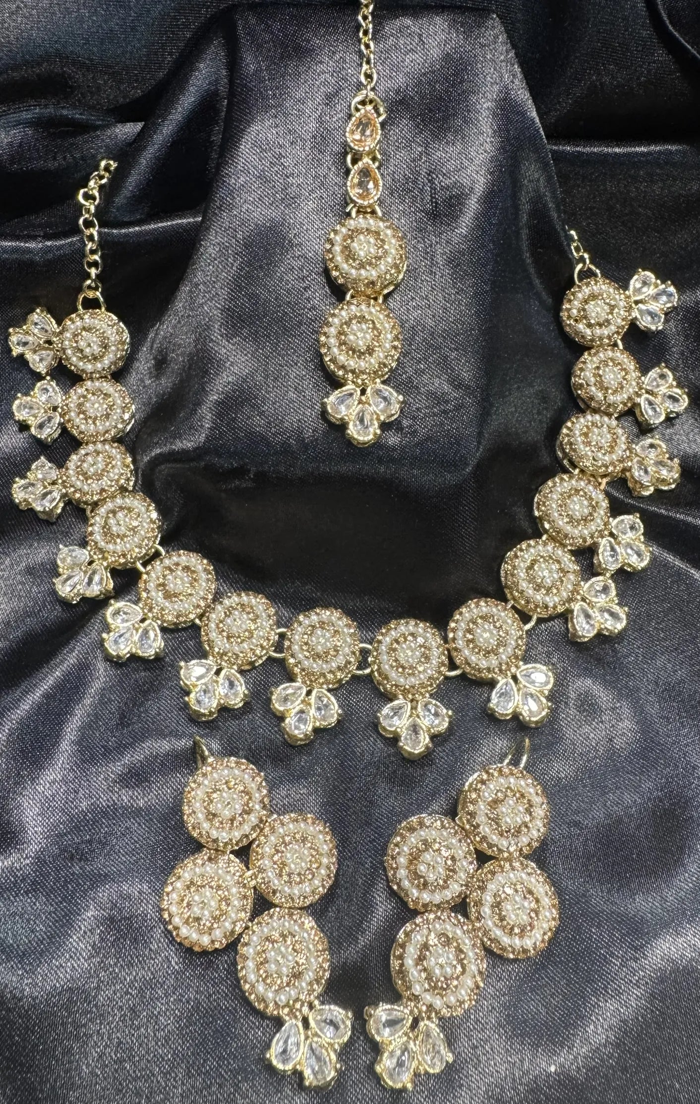 Gold necklace and earrings set on a dark satin background