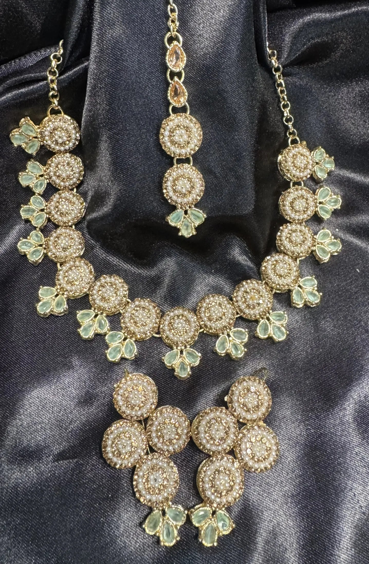 Gold and mint jewelry set on a dark satin background