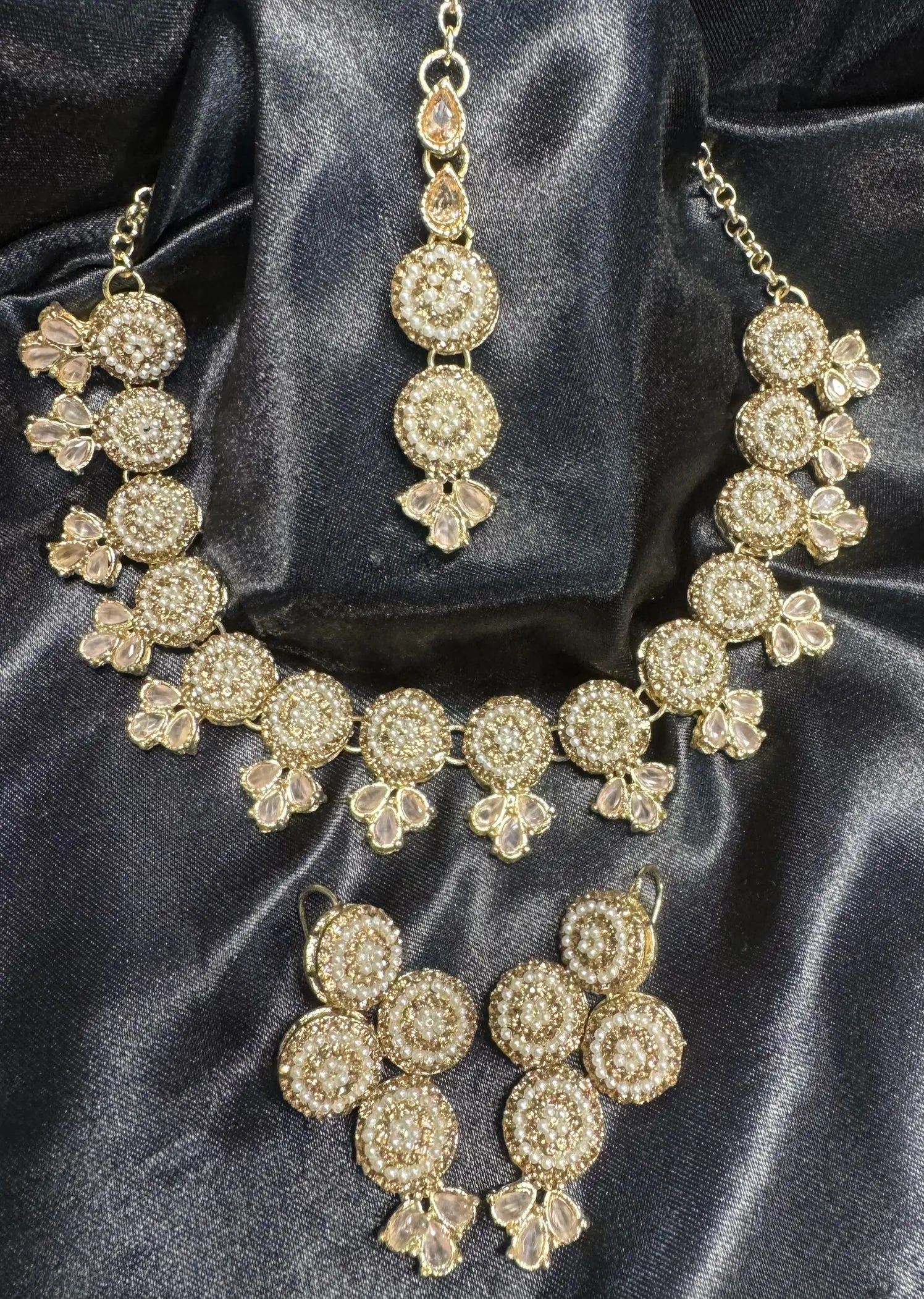 Gold necklace and earrings set on a dark satin background