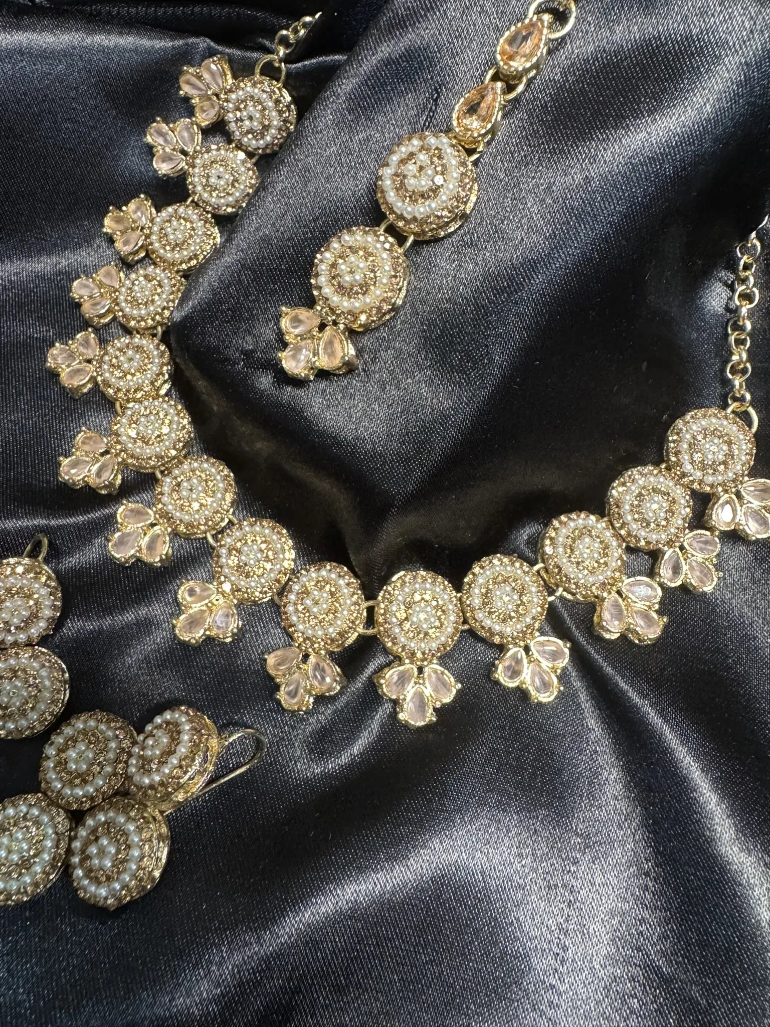 Gold necklace with intricate design on a dark satin background