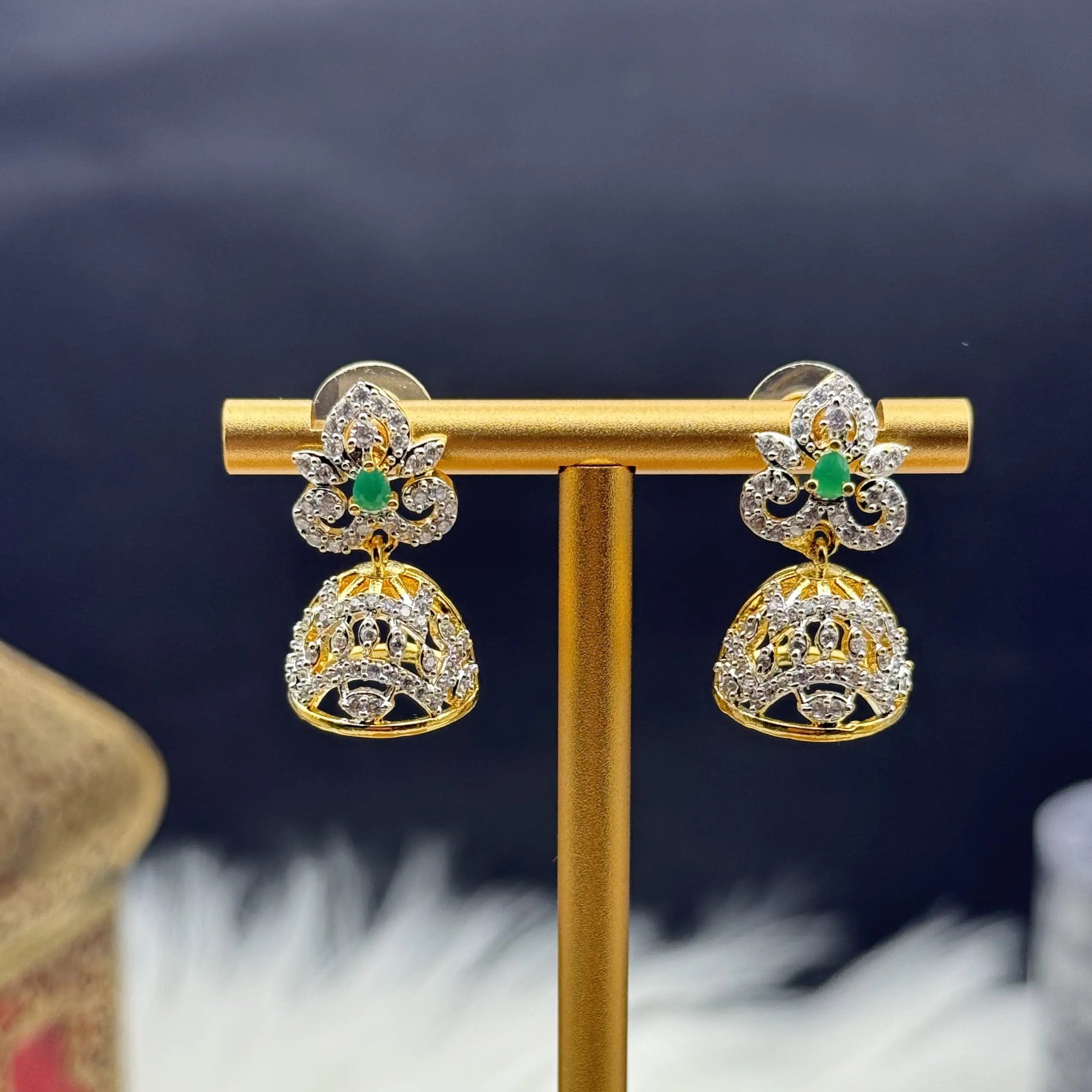 Gold plated Pakistani style jhumka earrings with green gemstones on a gold stand against a dark background