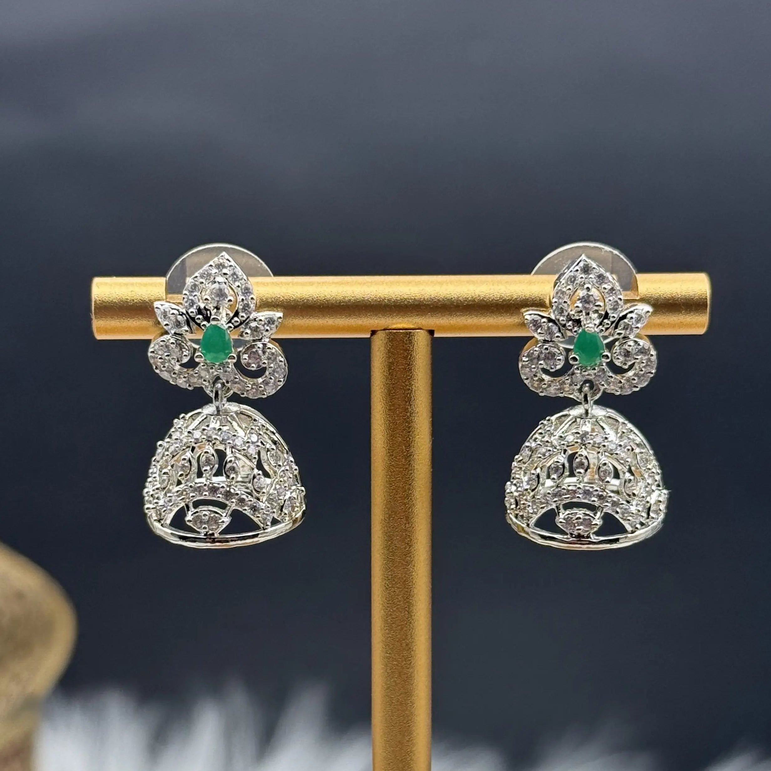 Pair of silver Pakistani style jhumka earrings with green gemstones on a gold stand against a dark background