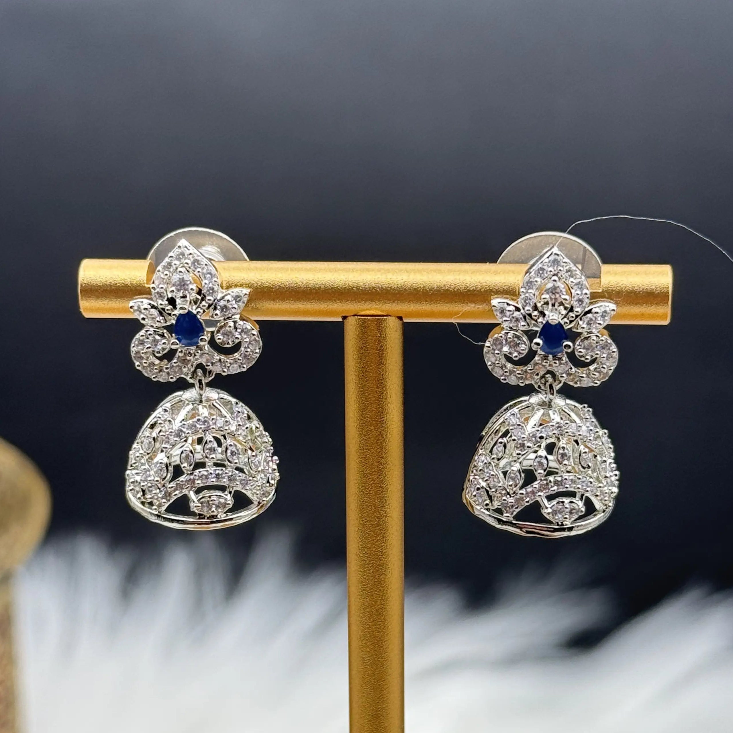 Silver Pakistani style jhumka earrings with blue gemstones on a gold stand against a dark background