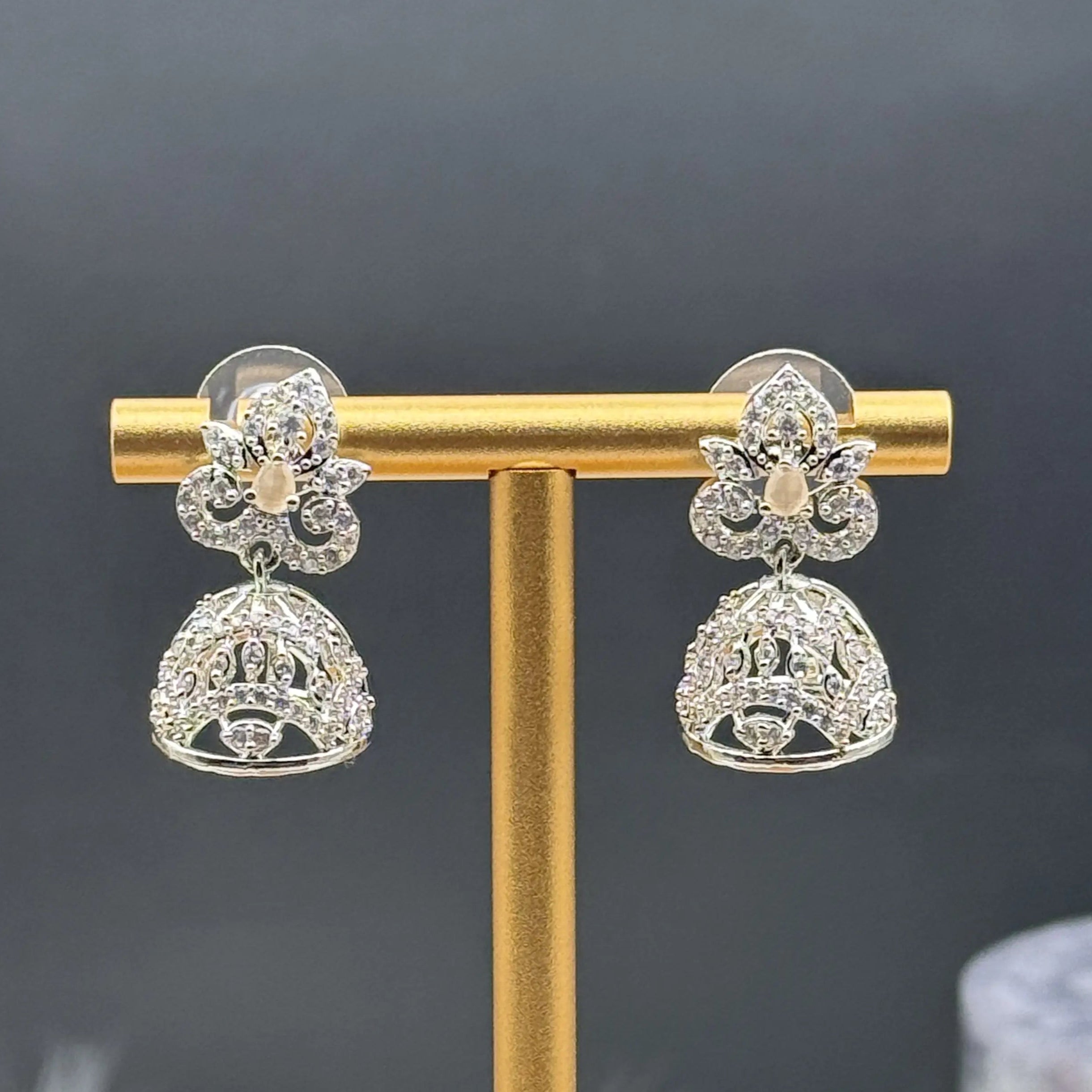 Pair of silver Pakistani style jhumka earrings with peach gemstones on a gold stand against a dark background