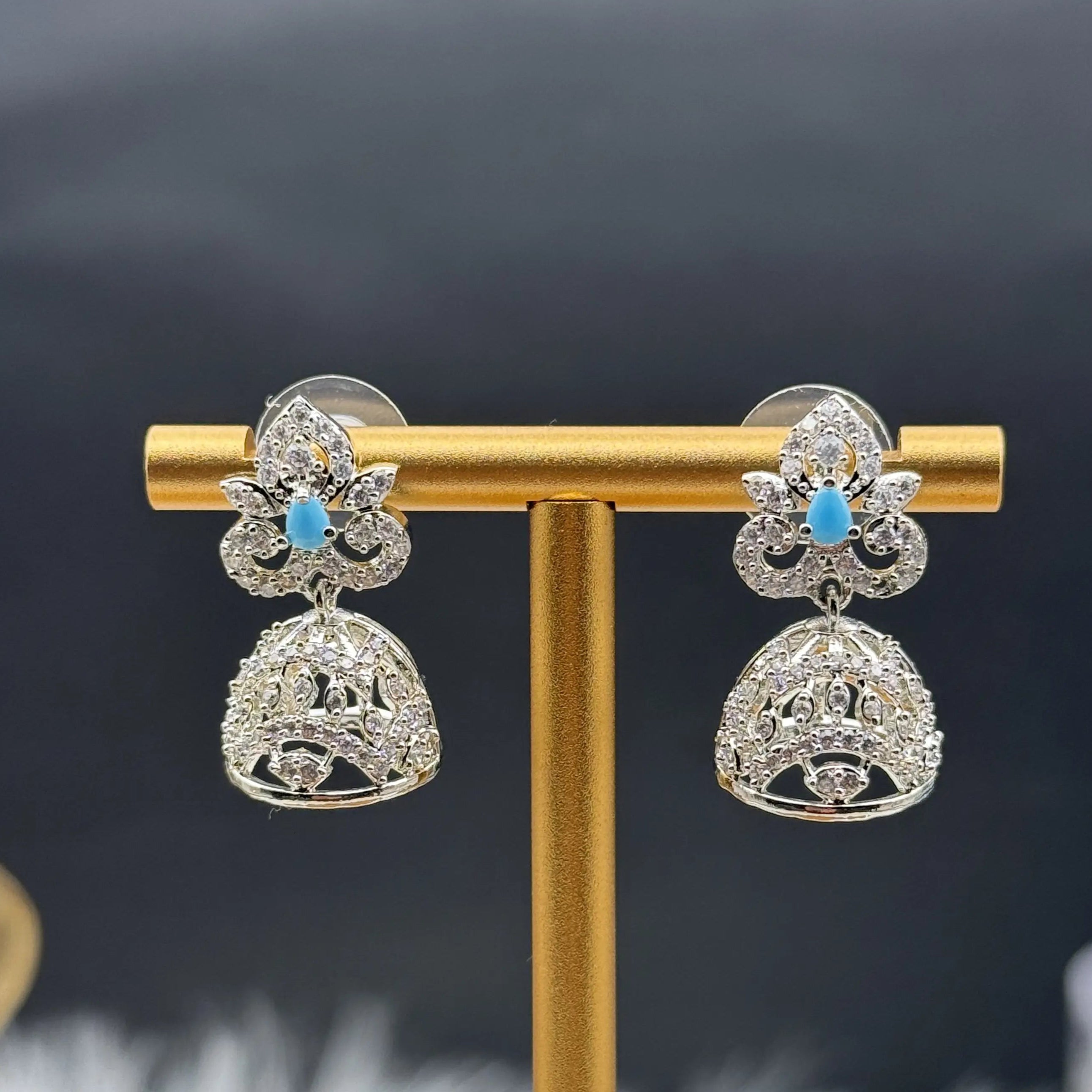 Silver Pakistani style jhumka earrings with turquoise stones on a gold stand against a dark background