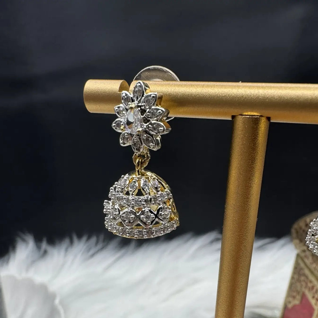 Pakistani style jhumka earring with clear gemstones and a gold base against a dark background.