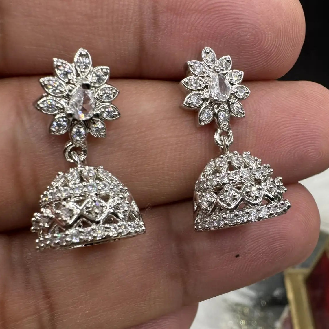 another view of Pair of Pakistani style jhumka earrings with clear gemstones and a silver base held between fingers with a blurred background 