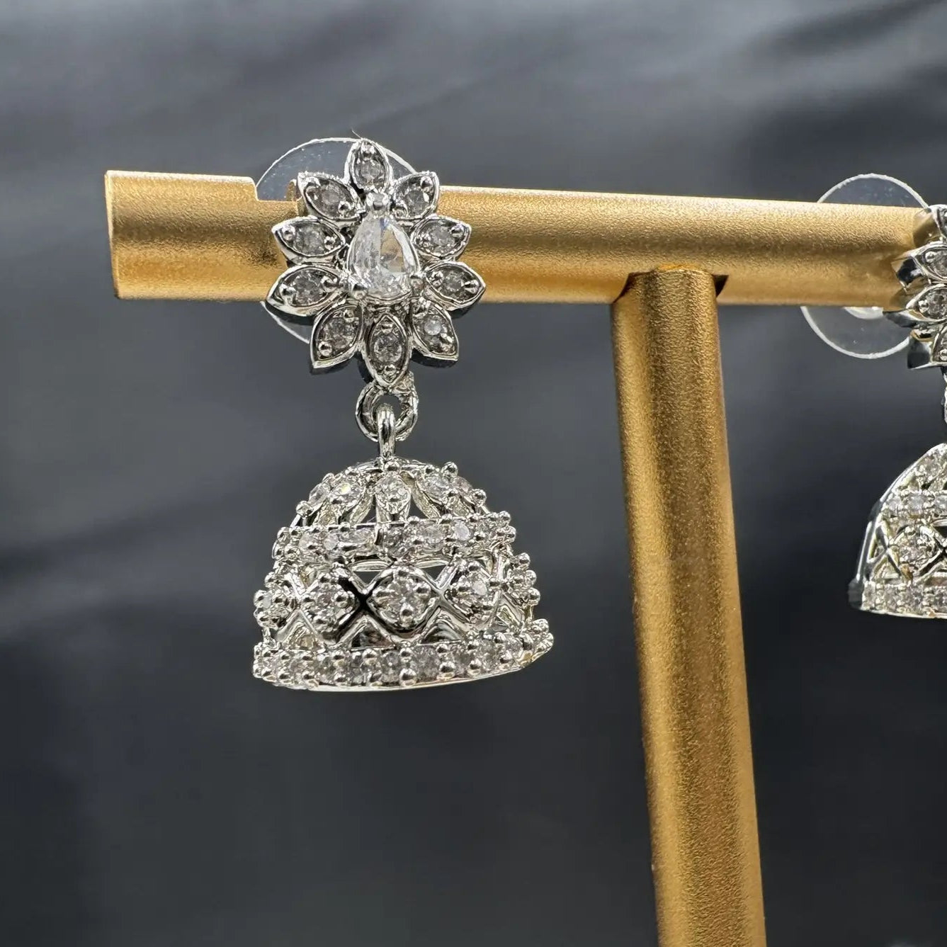 Silver jhumka earrings on a gold stand against a dark background