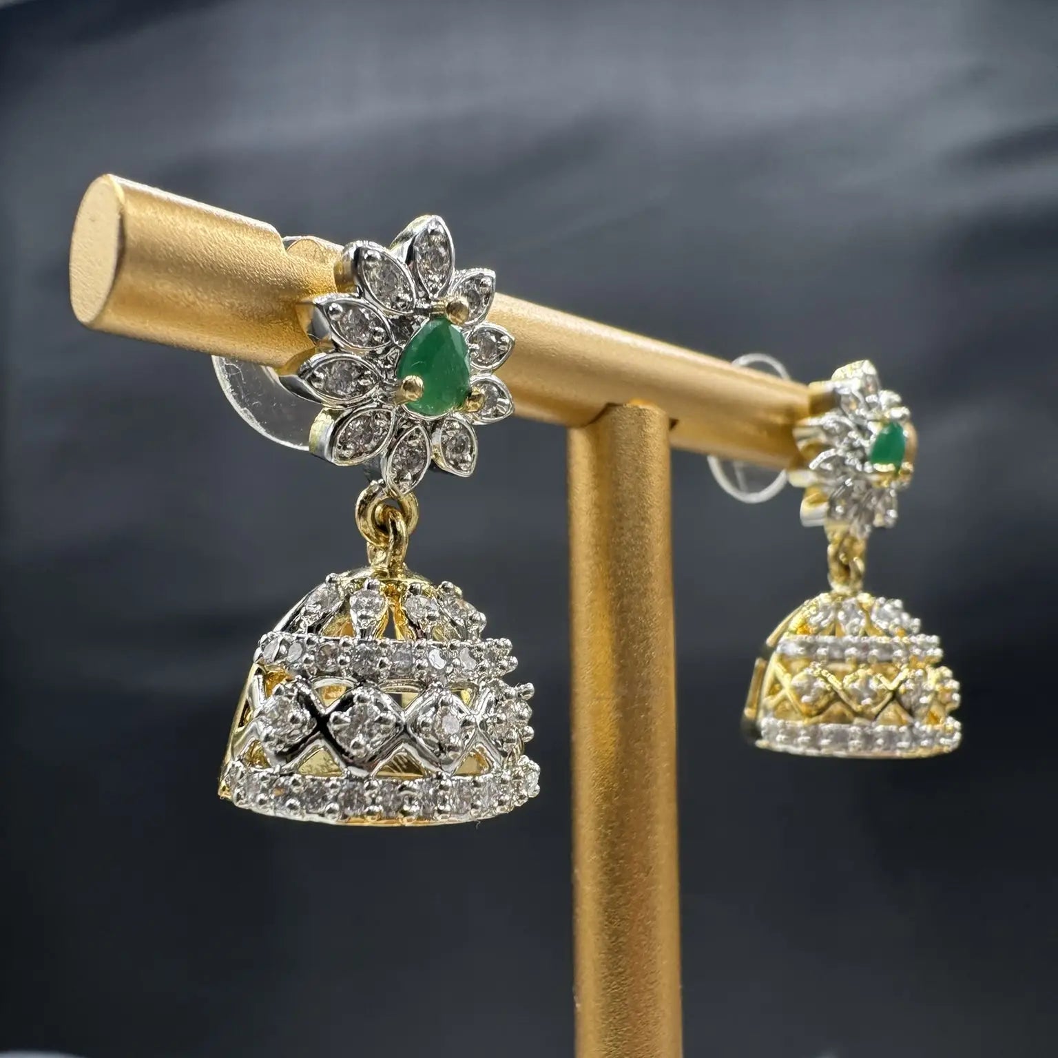 Pair of Pakistani style jhumka earrings with emerald gemstones and a gold base with a blurred background 