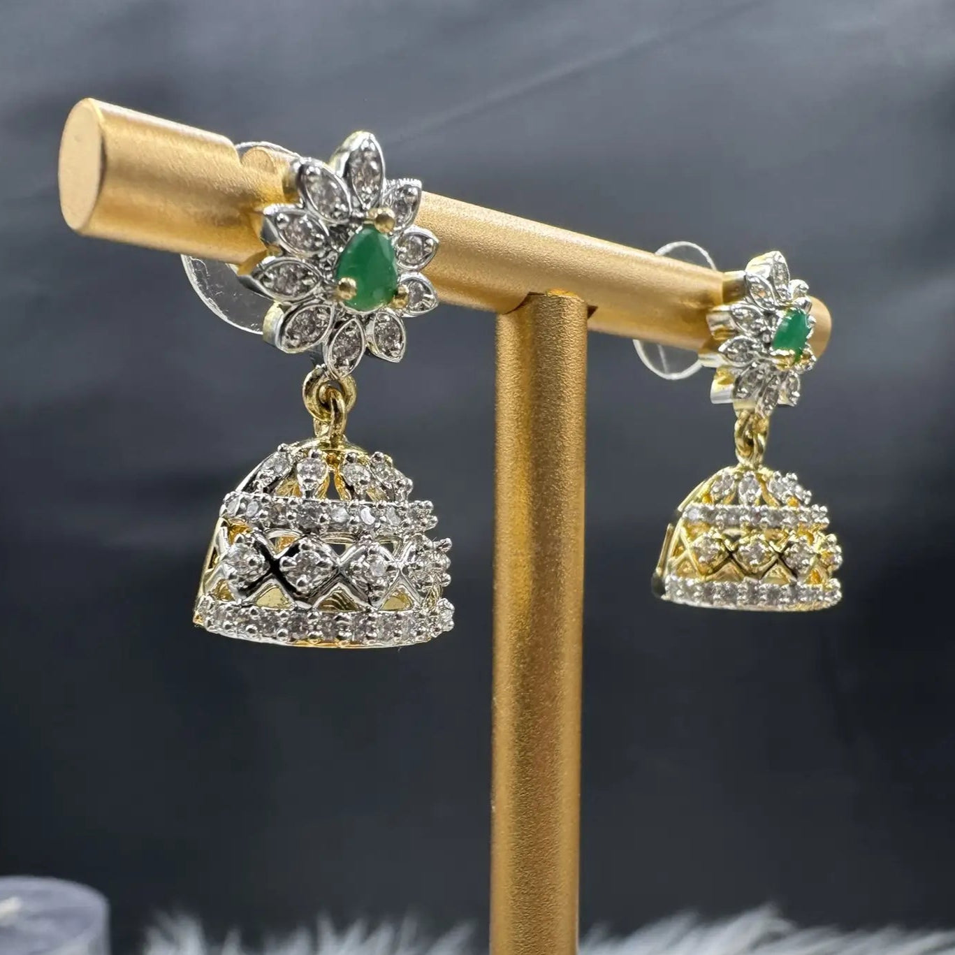 left side view of Pair of Pakistani style jhumka earrings with emerald gemstones and a gold base with a blurred background 