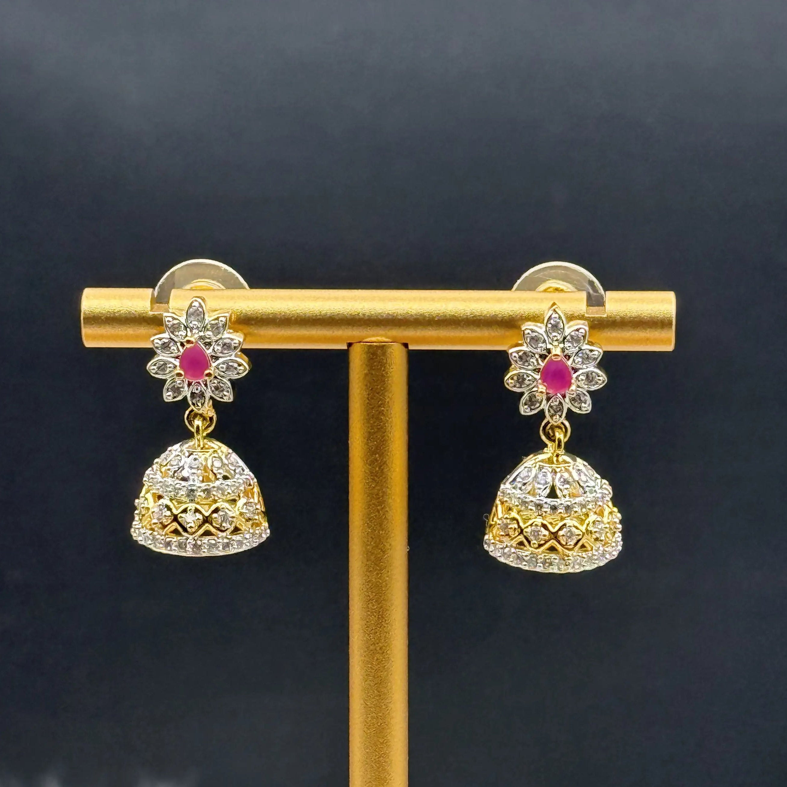Pair of Pakistani style jhumka earrings with hotpink gemstones and a gold base on a stand
