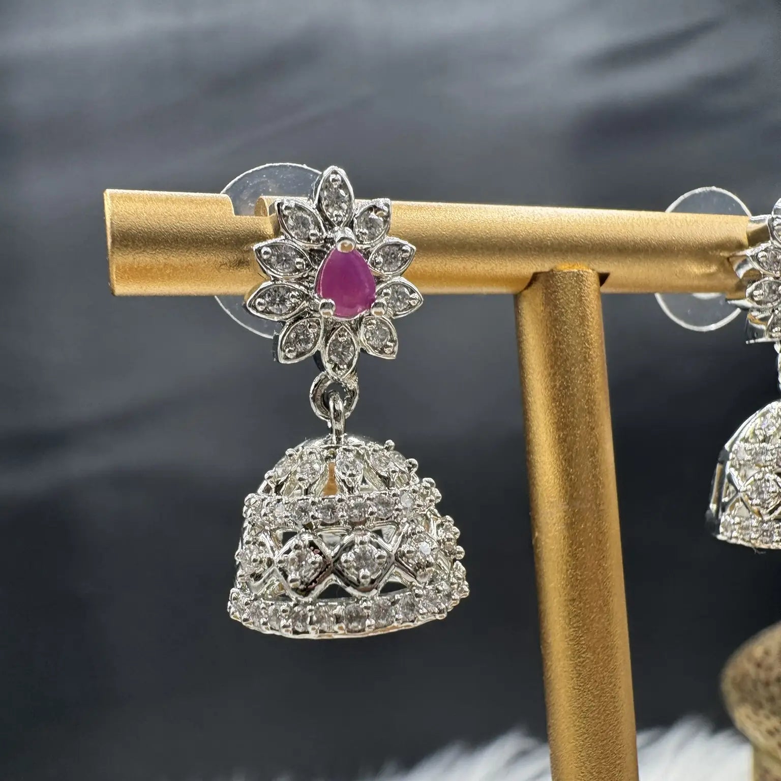 Pair of Pakistani style jhumka earrings with hotpink gemstones and a silver base with a blurred background 