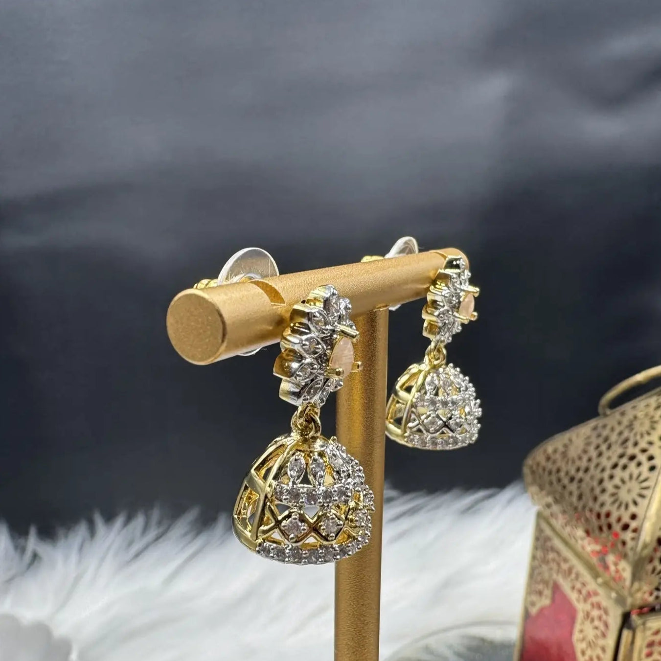 side view of Pair of Pakistani style jhumka earrings with peach gemstones and a gold base with a blurred background 
