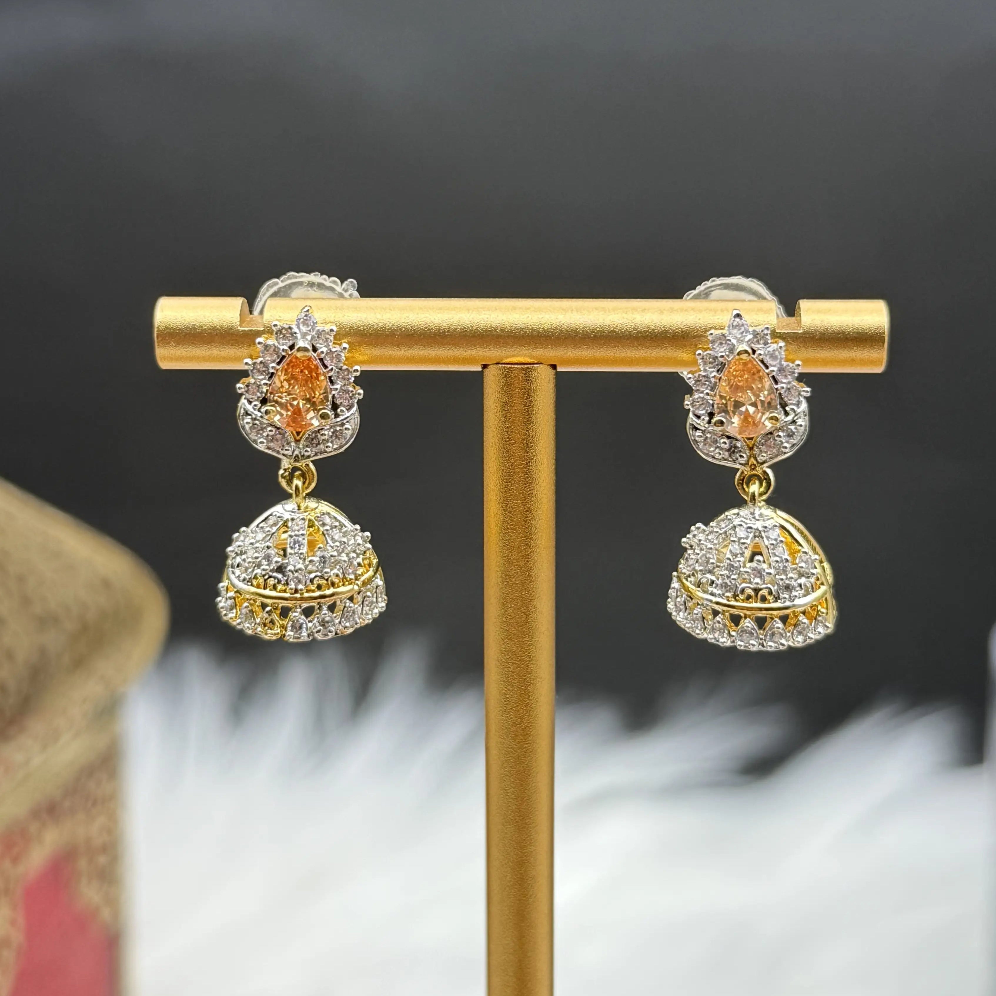 Pair of Pakistani style jhumka earrings with champagne gemstones and a gold base on a gold stand against a dark background
