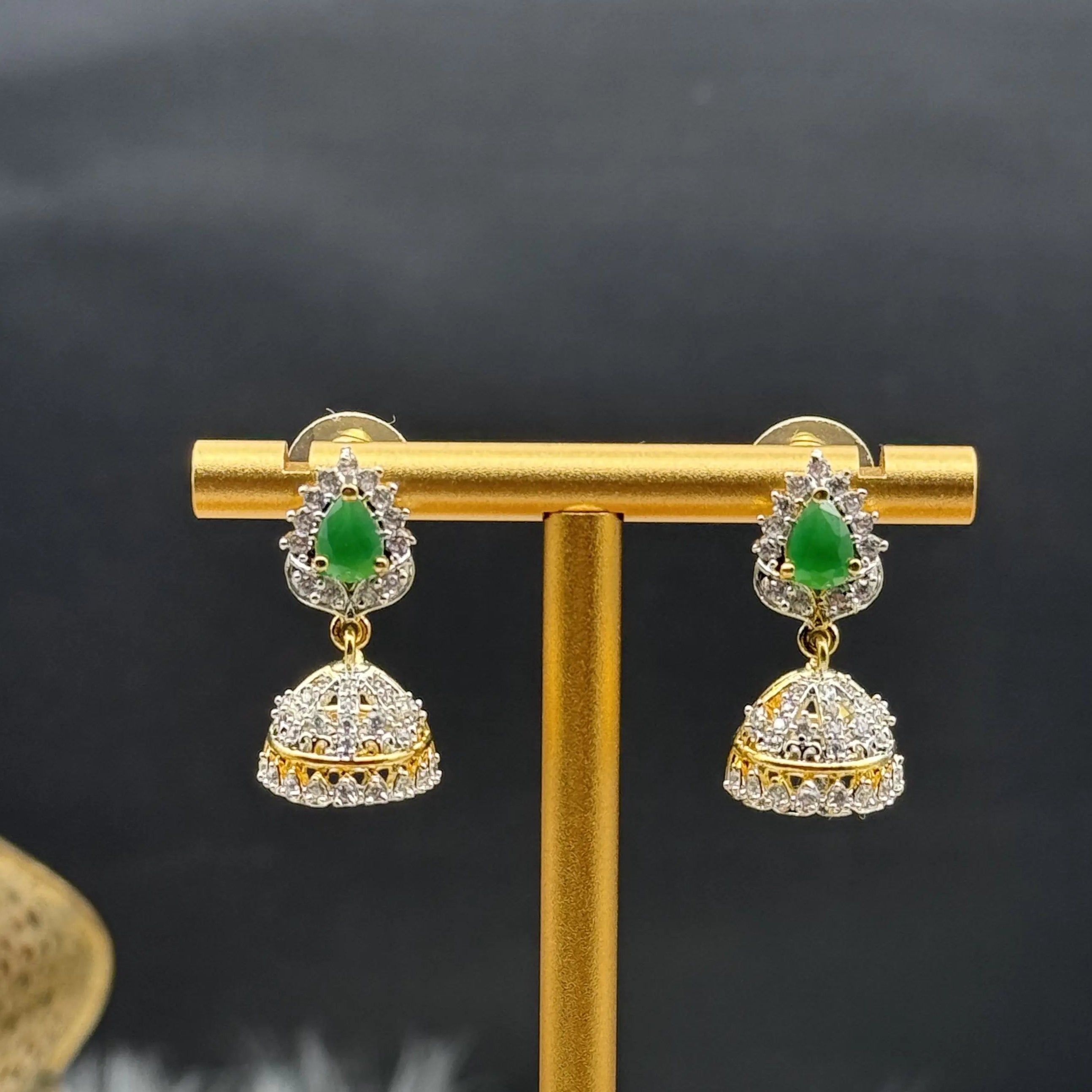 Pair of Pakistani style jhumka earrings with green gemstones and a gold base on a gold stand against a dark background