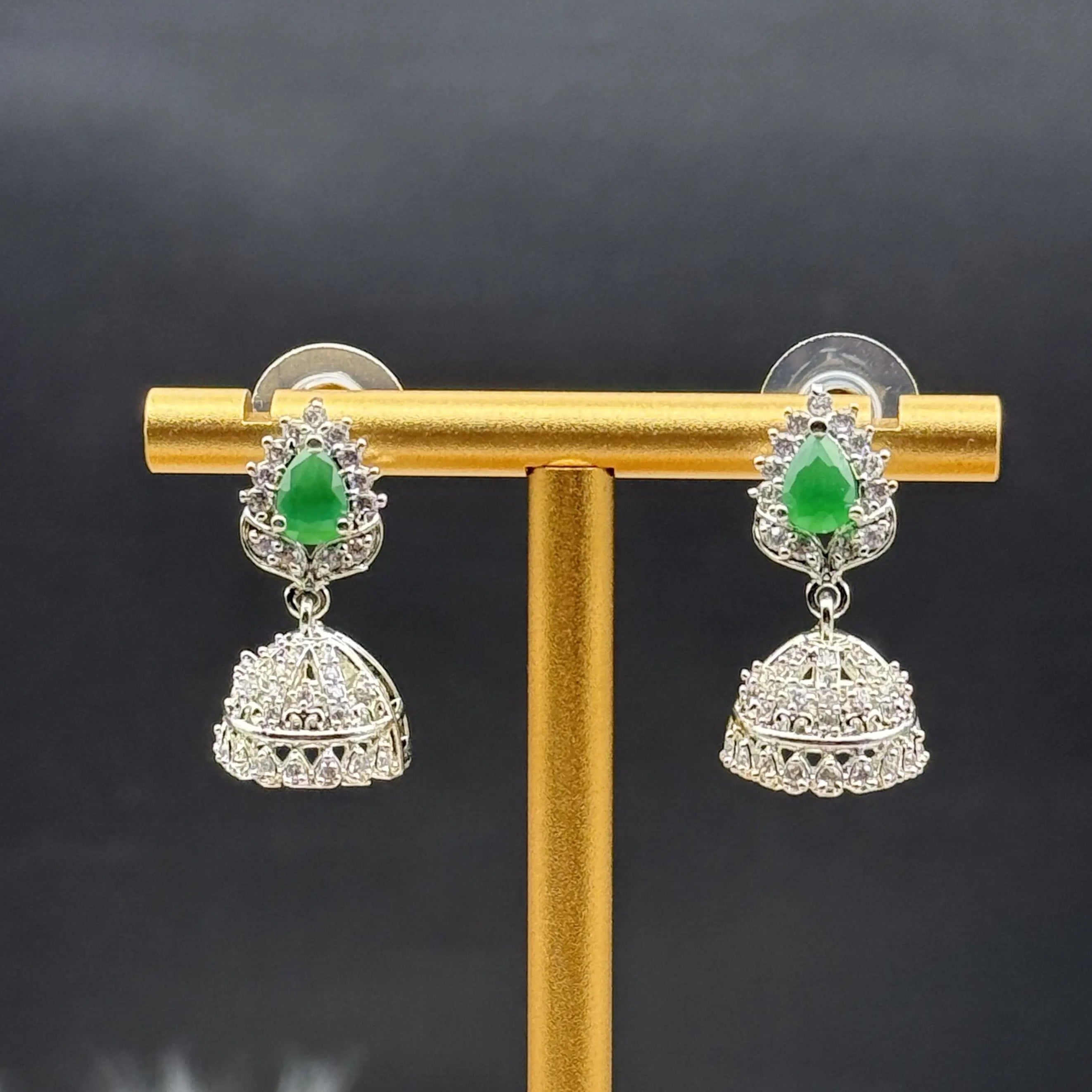 Pair of Pakistani style jhumka earrings with green gemstones on a gold stand against a dark background