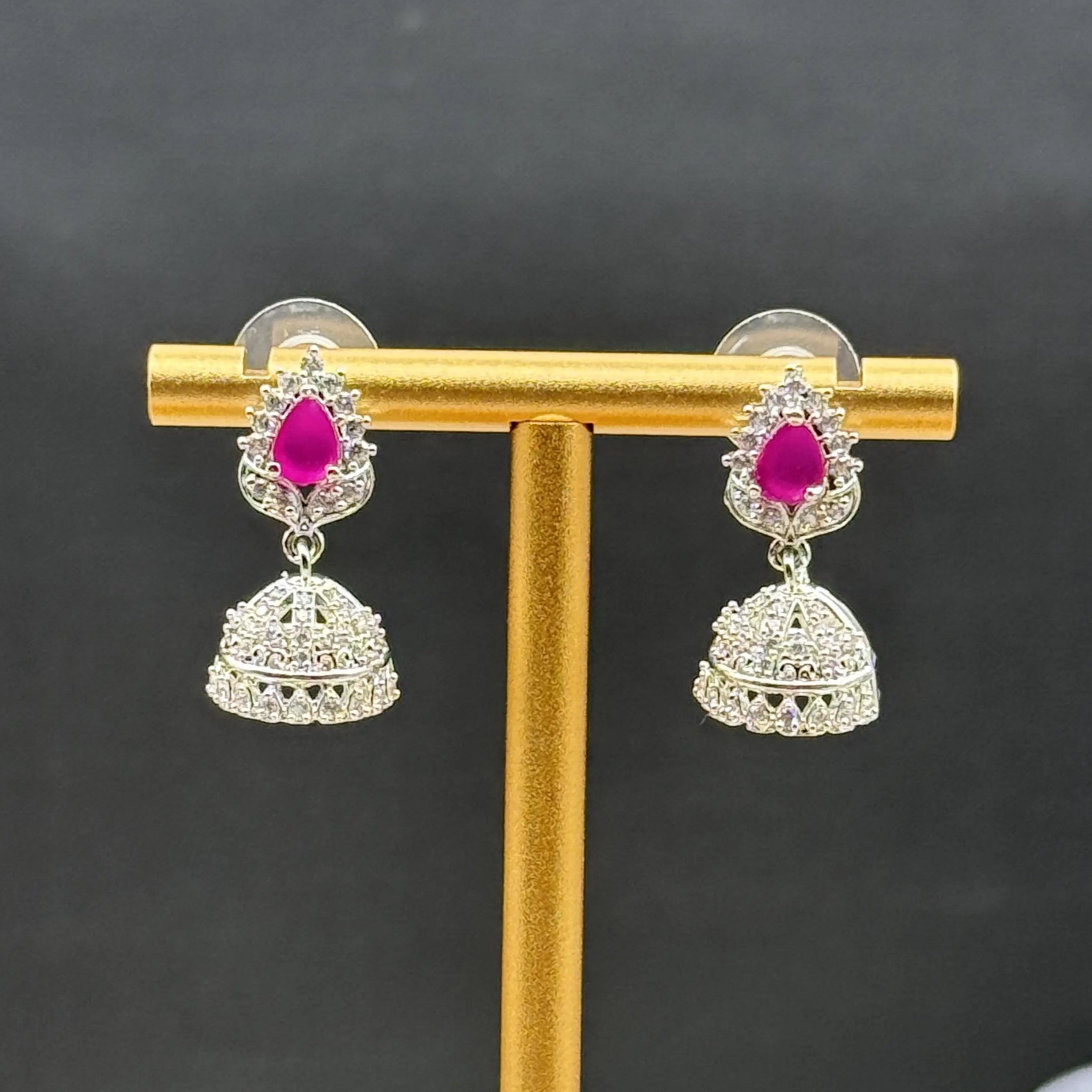 Pair of Pakistani style jhumka earrings with hotpink gemstones on a gold stand against a dark background