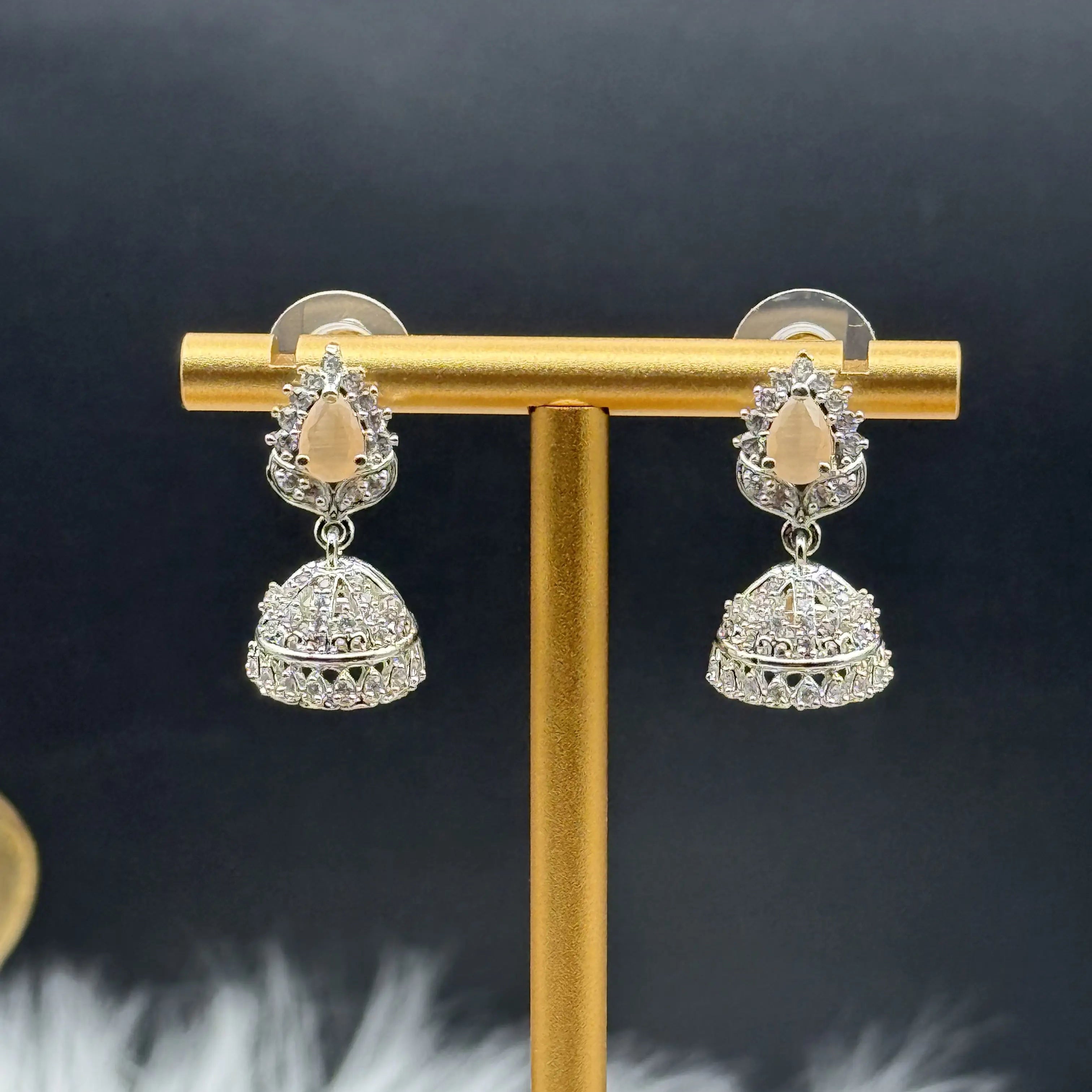 Pair of Pakistani style jhumka earrings with peach gemstones on a gold stand against a dark background
