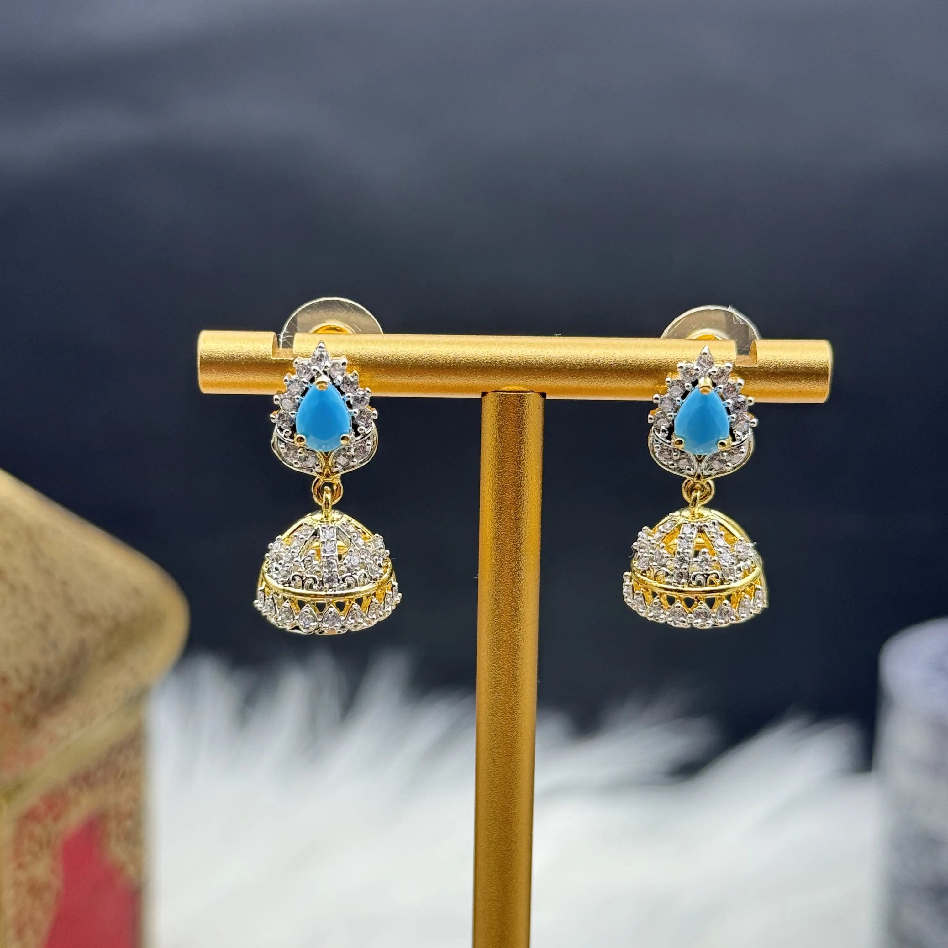 Pair of Pakistani style jhumka earrings with sky blue gemstones and a gold base on a gold stand against a dark background