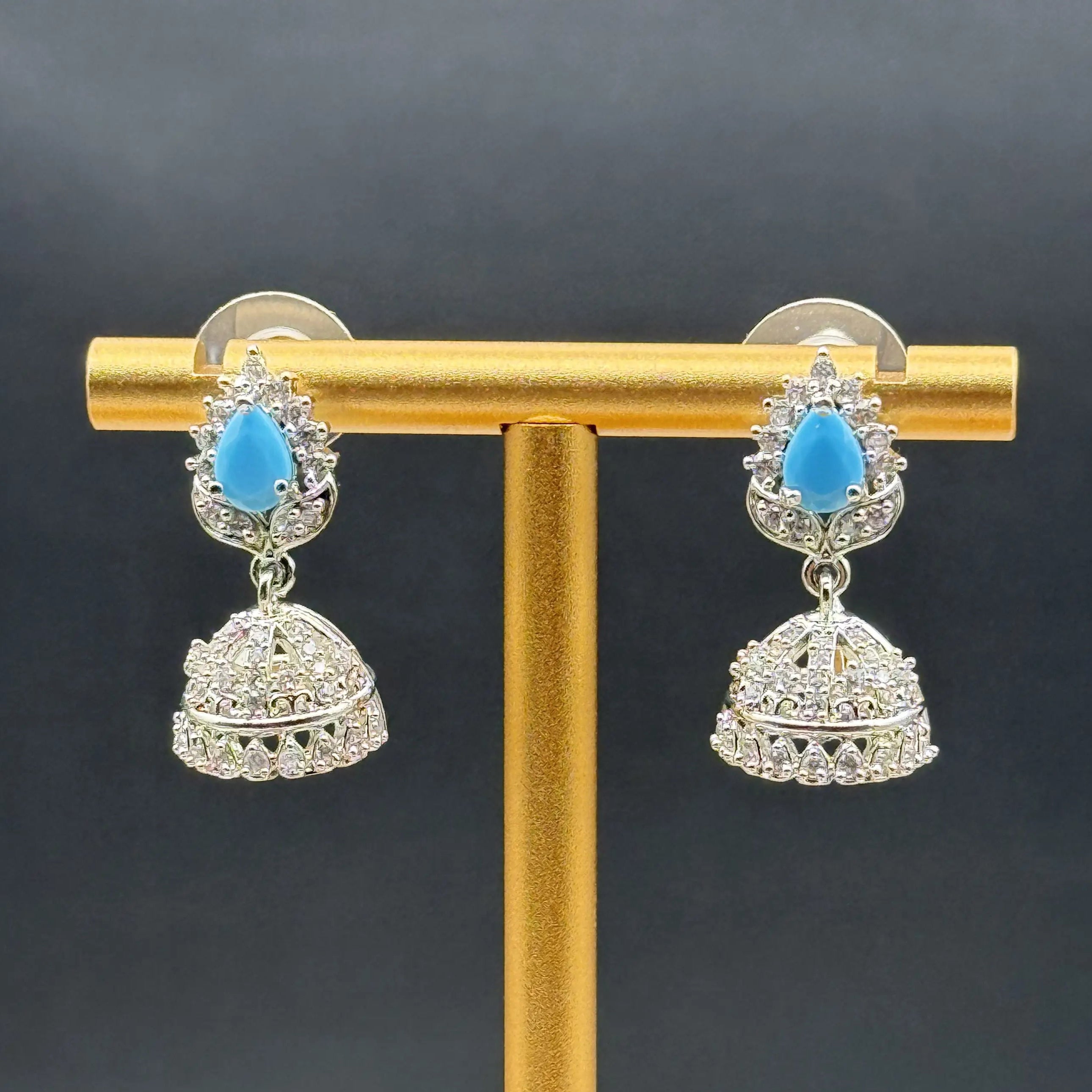 Pair of Pakistani style jhumka earrings with turquoise gemstones on a gold stand against a dark background