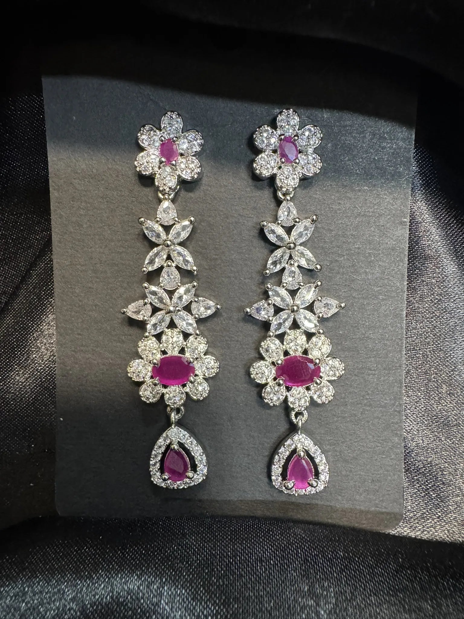 Pair of floral earrings with pink gemstones on a gray card against a black background