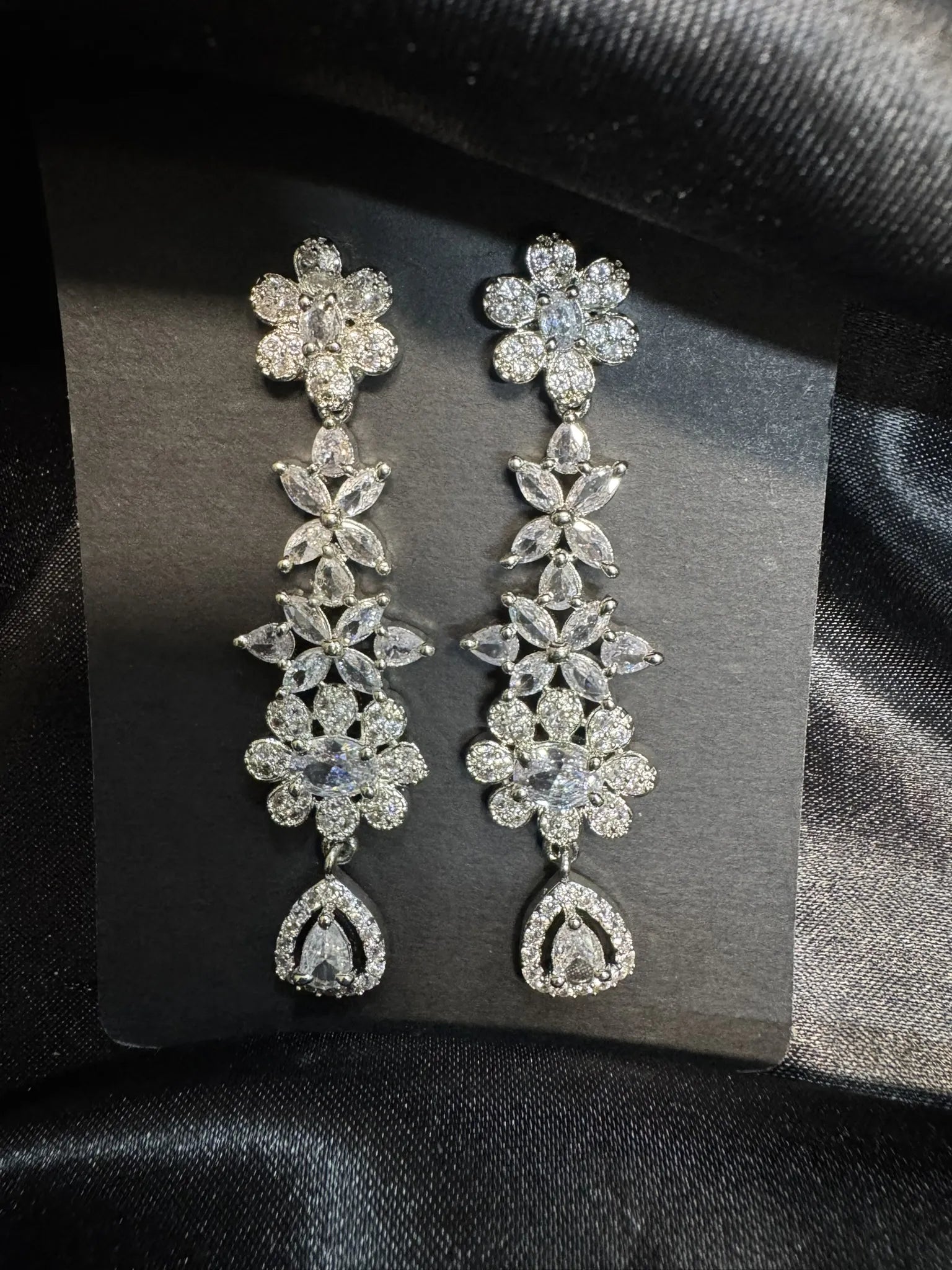 Pair of floral diamond earrings on a gray card with a black background