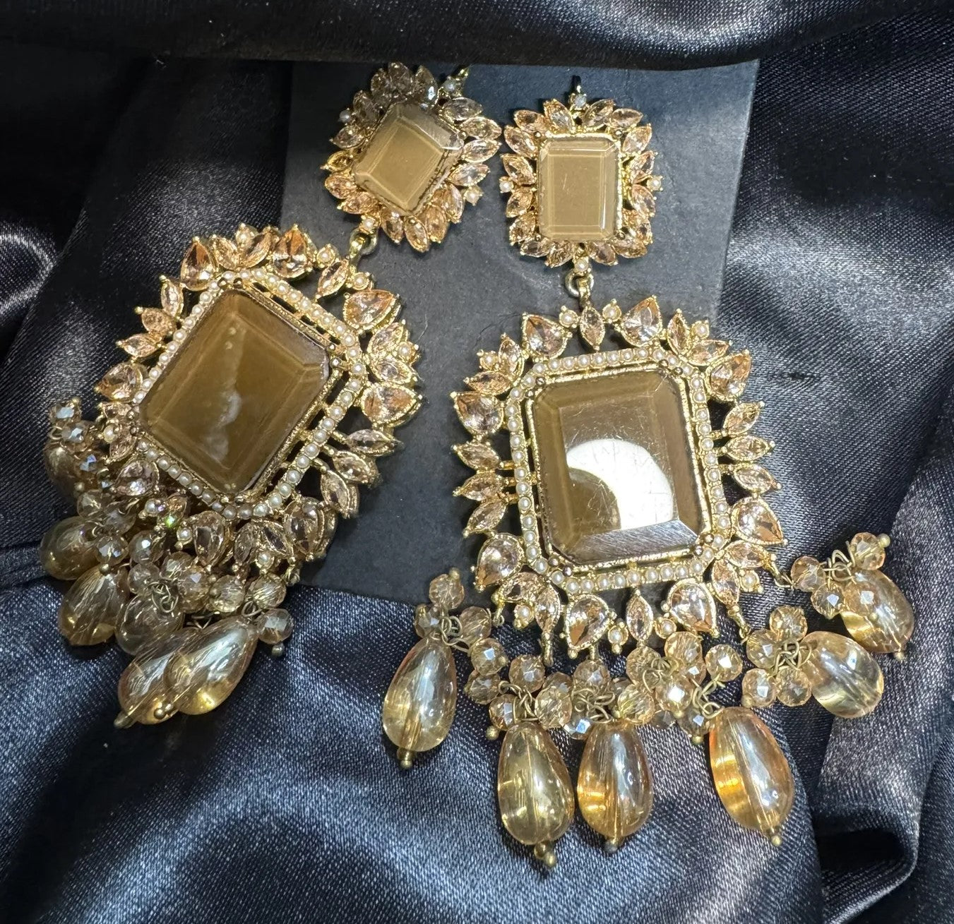 Ornate gold plated earrings with gemstones on a dark fabric background