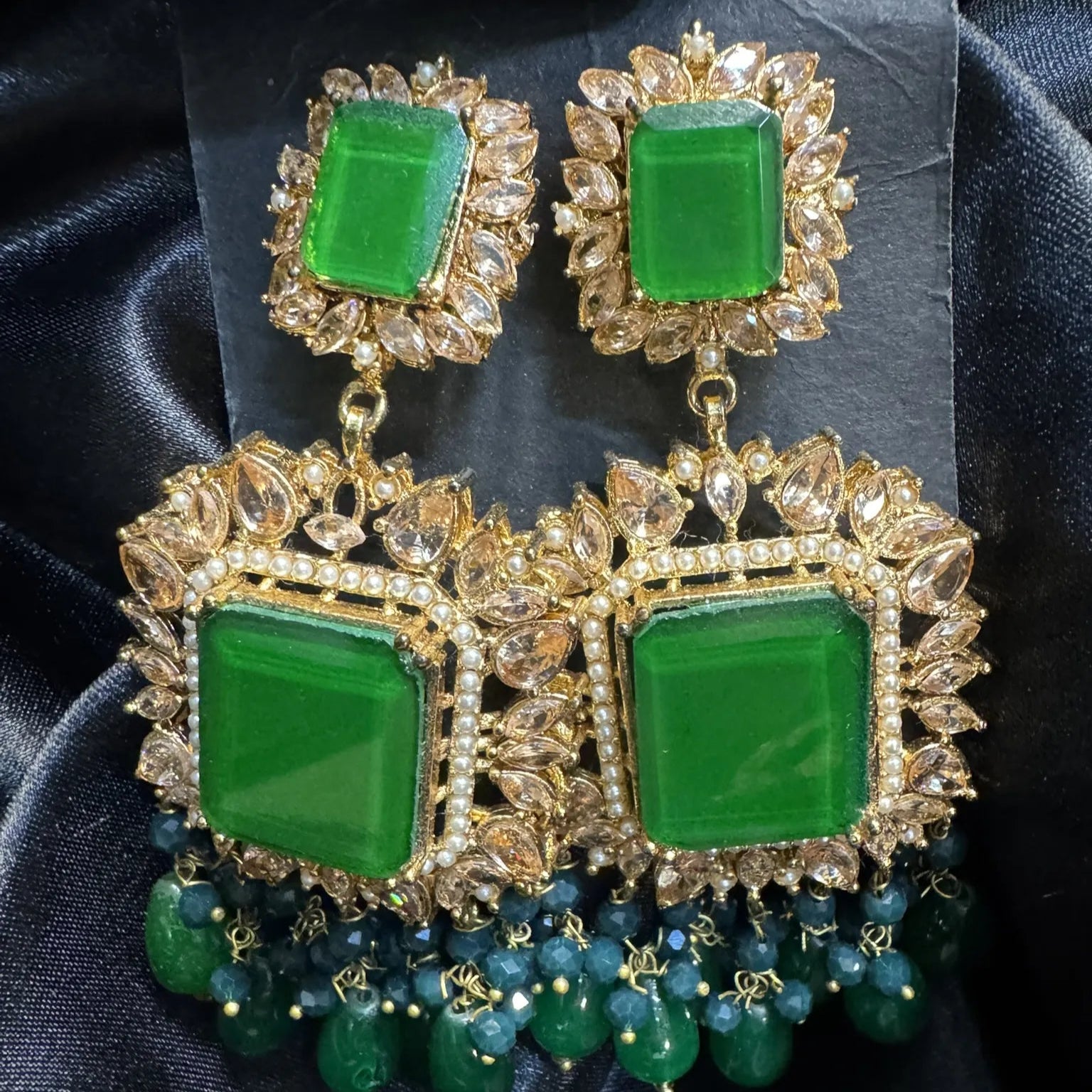 Green and gold earrings on a dark fabric background