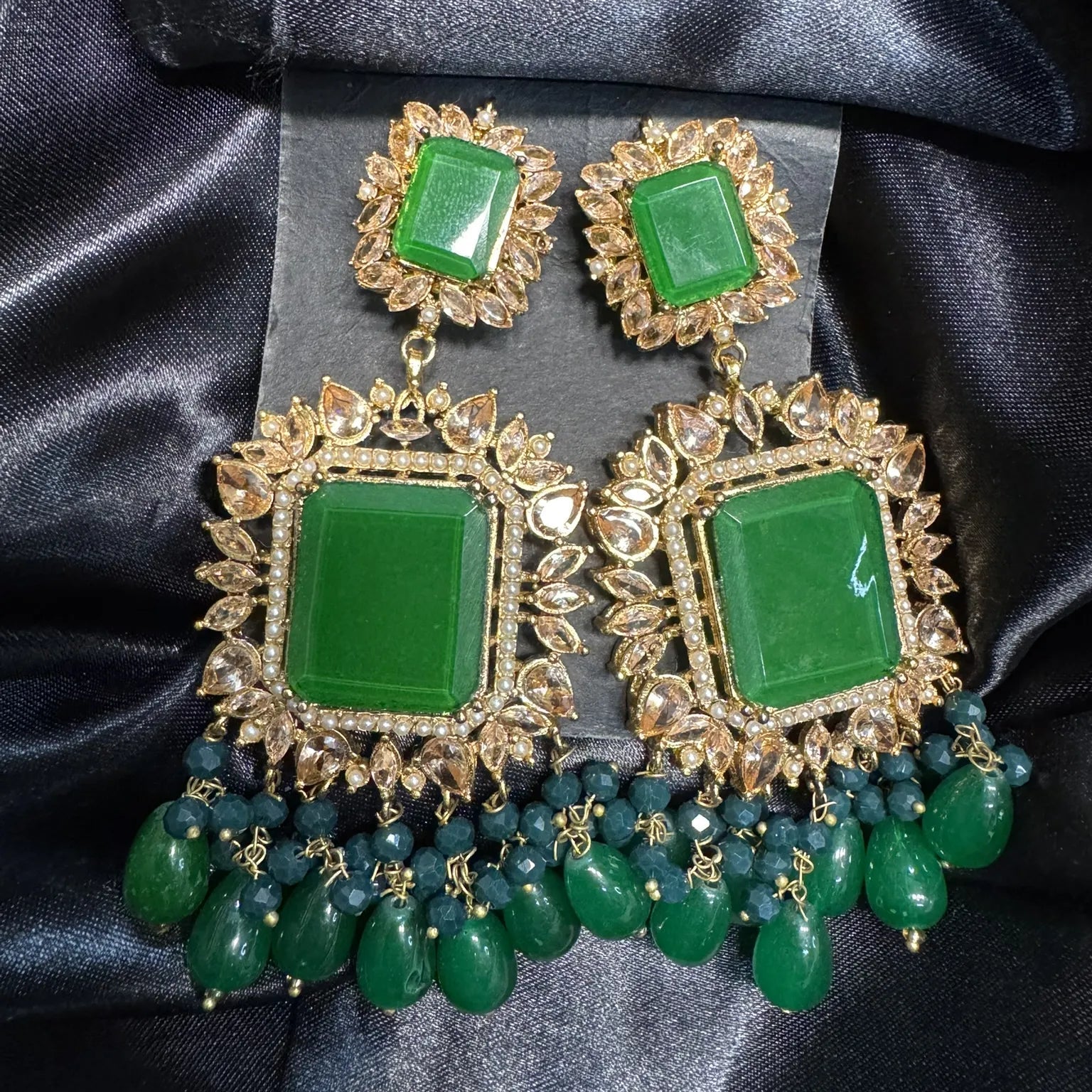 Green and gold earrings on a dark fabric background