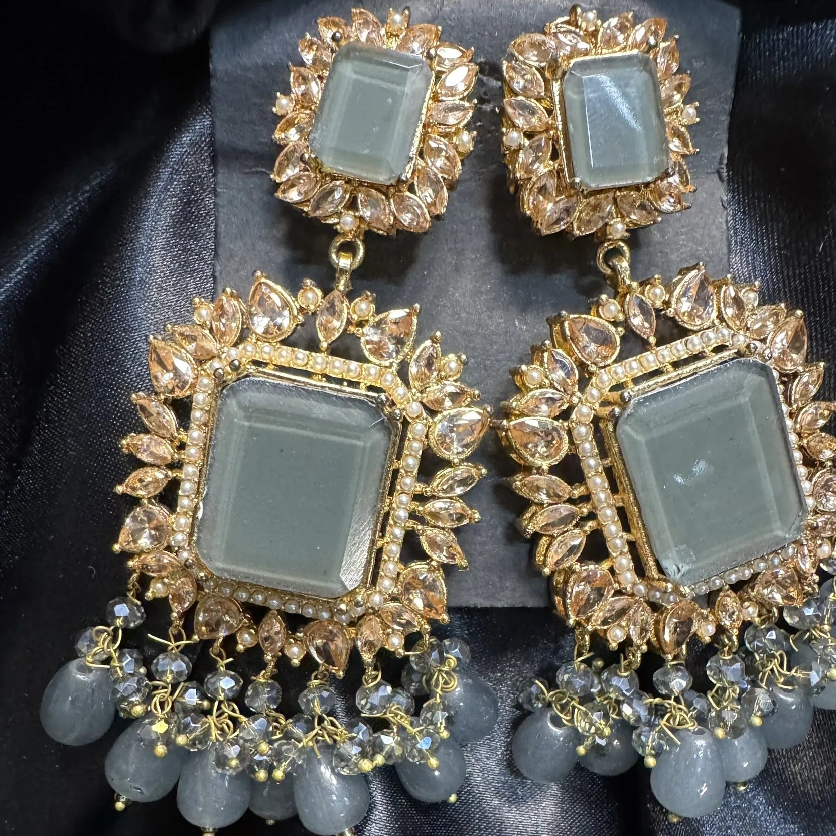 Pair of ornate earrings with gold frames and grey gemstones on a black background