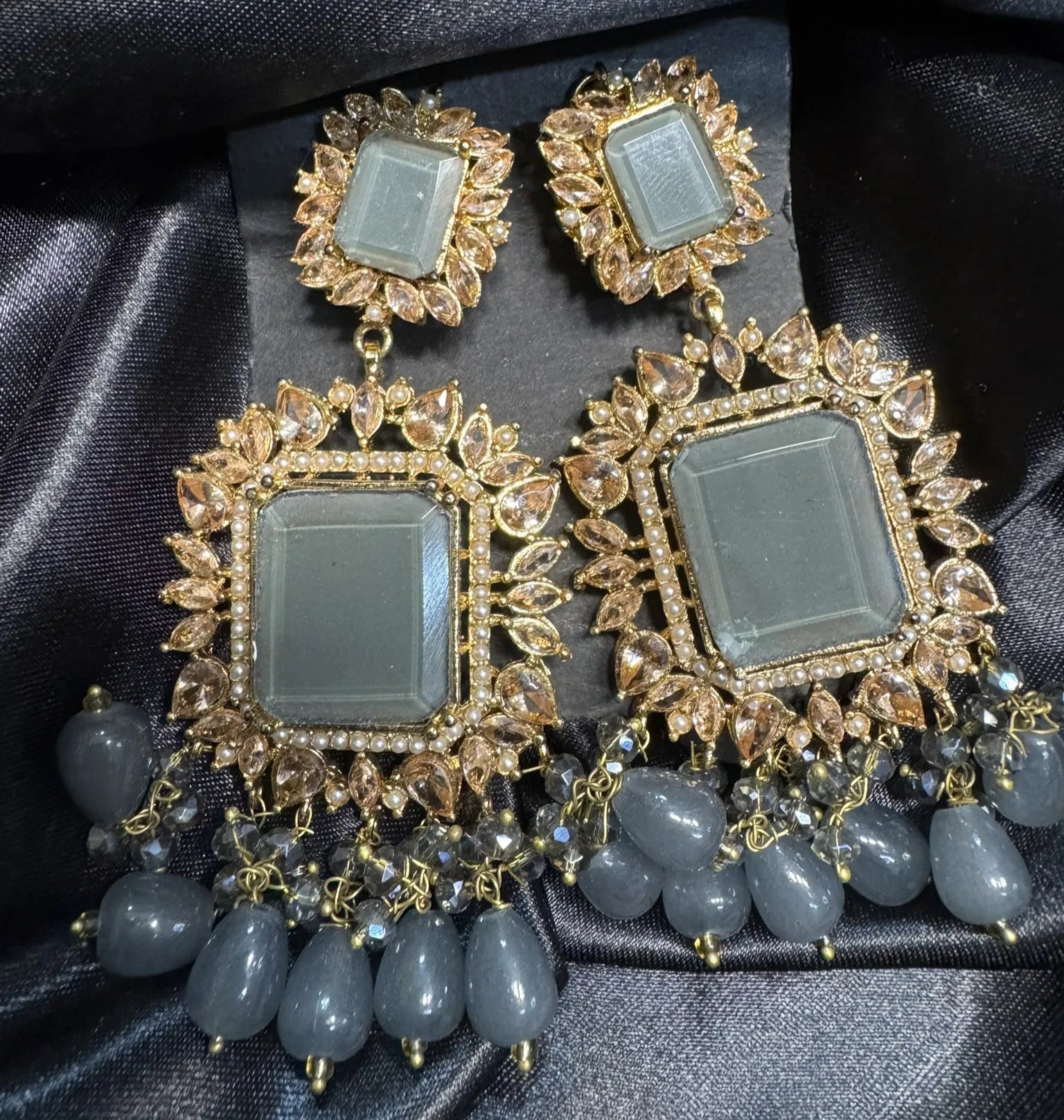 Pair of ornate earrings with gold and gray stones on a black satin background