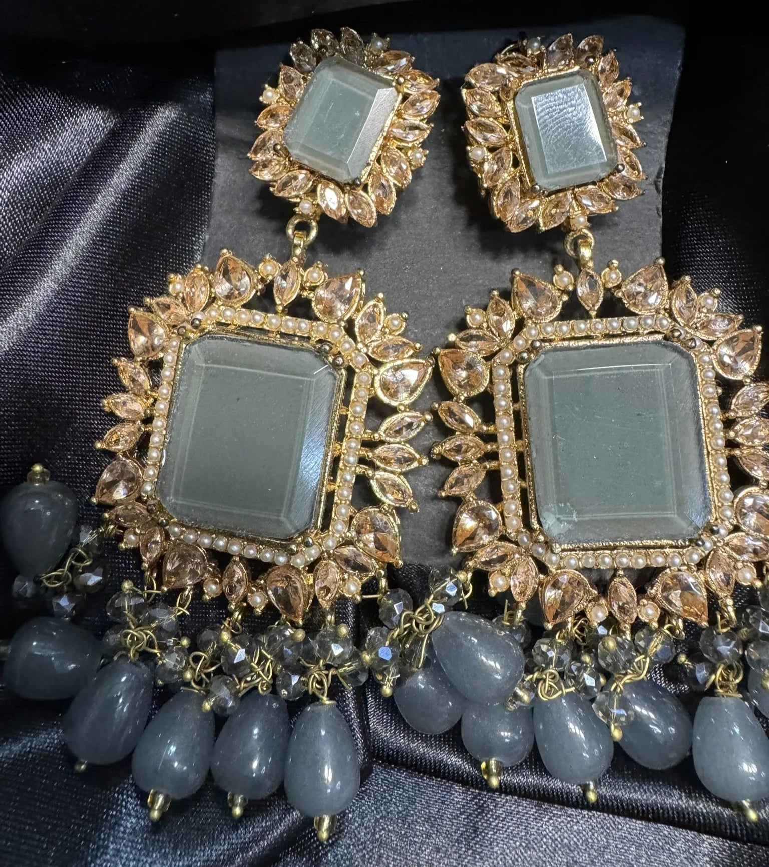 Ornate earrings with gold detailing and gray stones on a dark fabric background