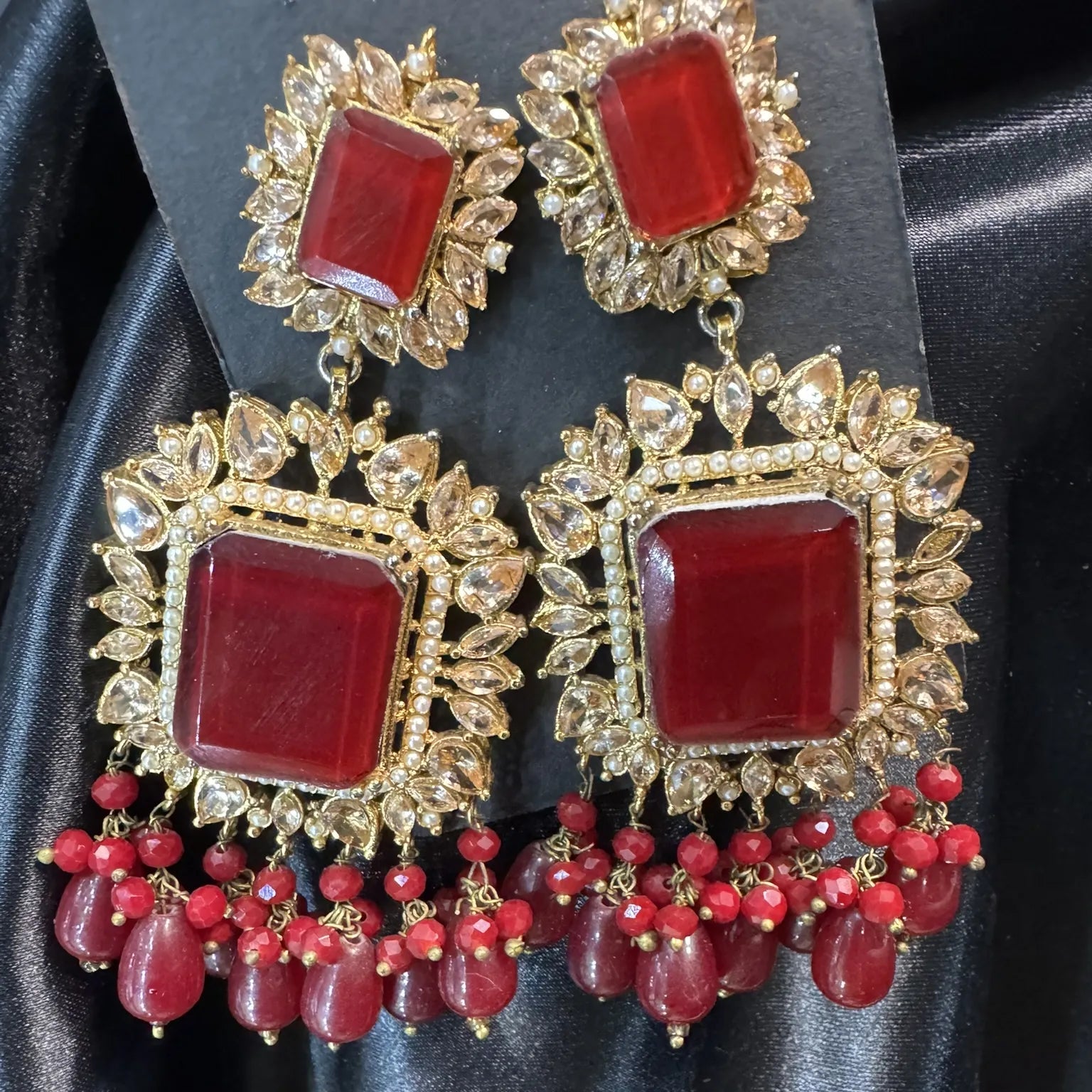 Pair of ornate earrings with red gemstones on a black satin background