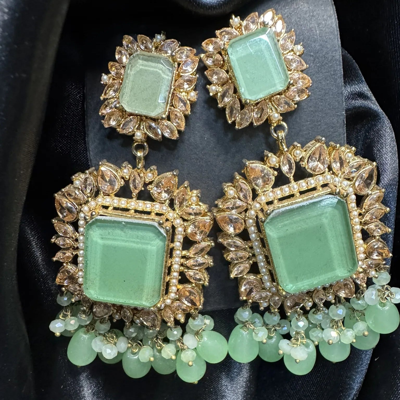 Mint square gemstone earrings with gold and green accents on a black satin background