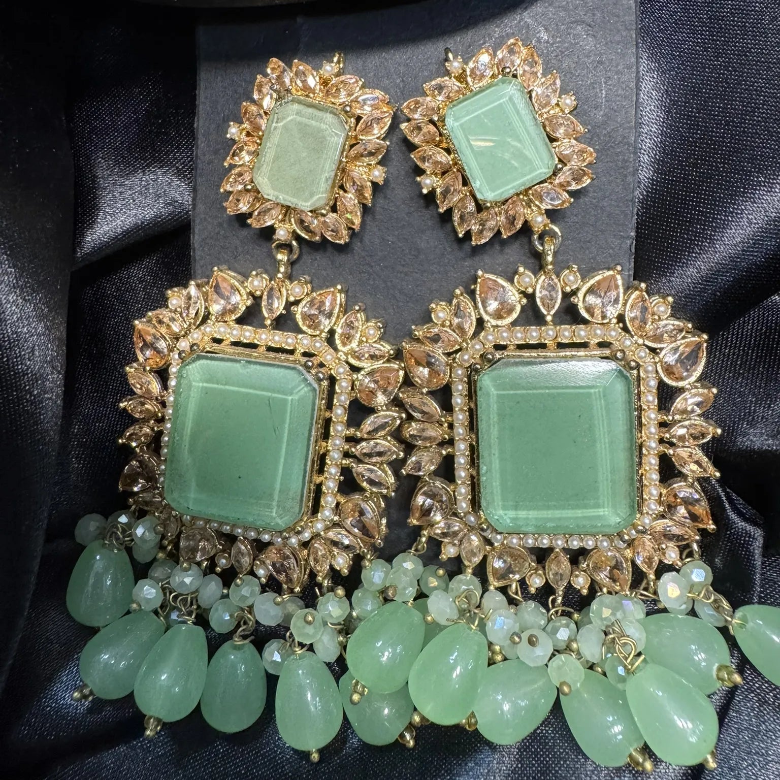 Pair of mint and gold-plated earrings on a black satin background