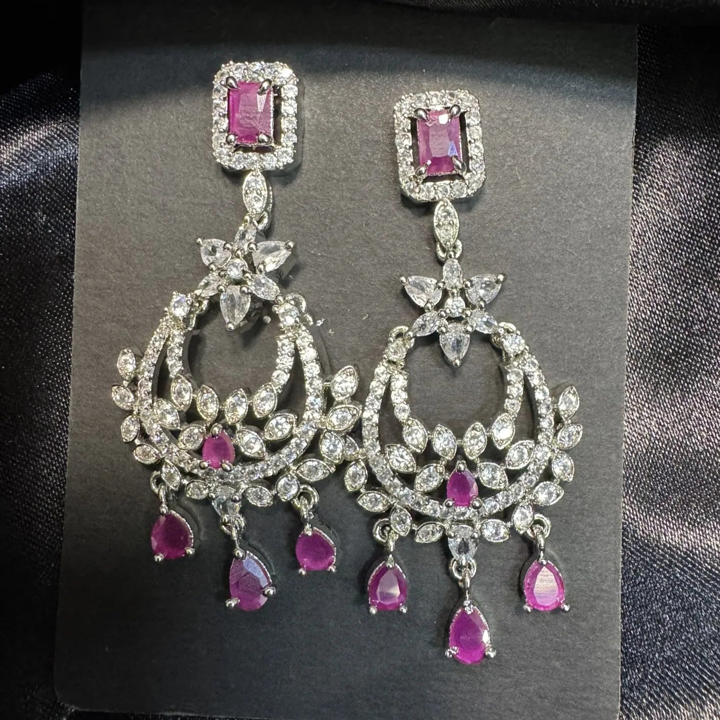 American Diamonds and hotpink gemstone earrings on a black card with a dark fabric background