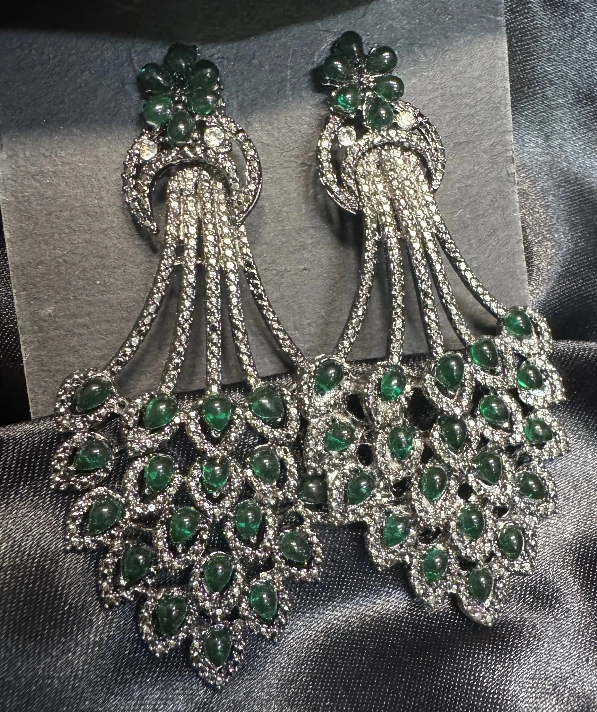 Pair of emerald and American diamond earrings on a gray fabric background