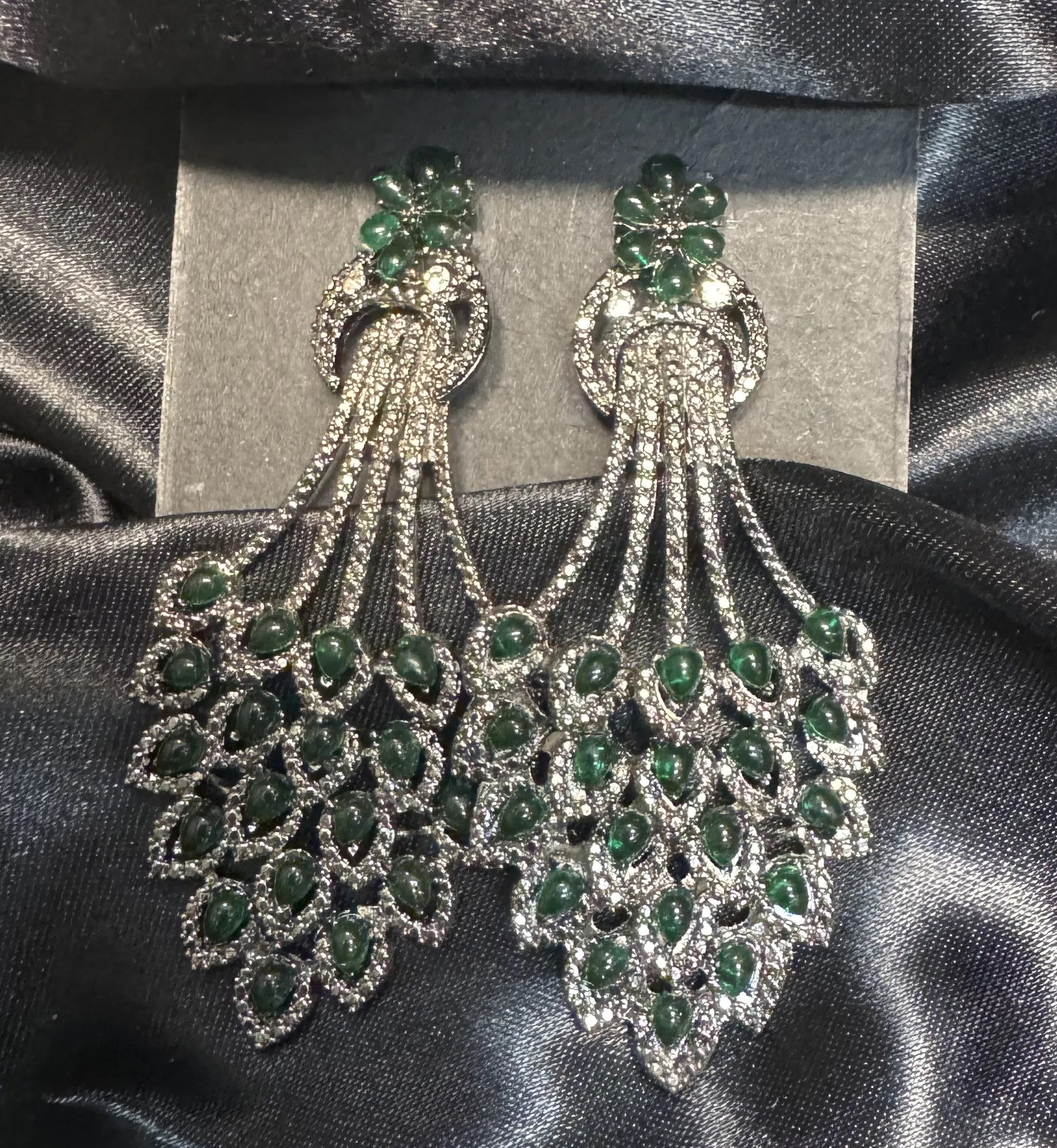 Pair of green gemstone earrings on a gray card with a black satin background