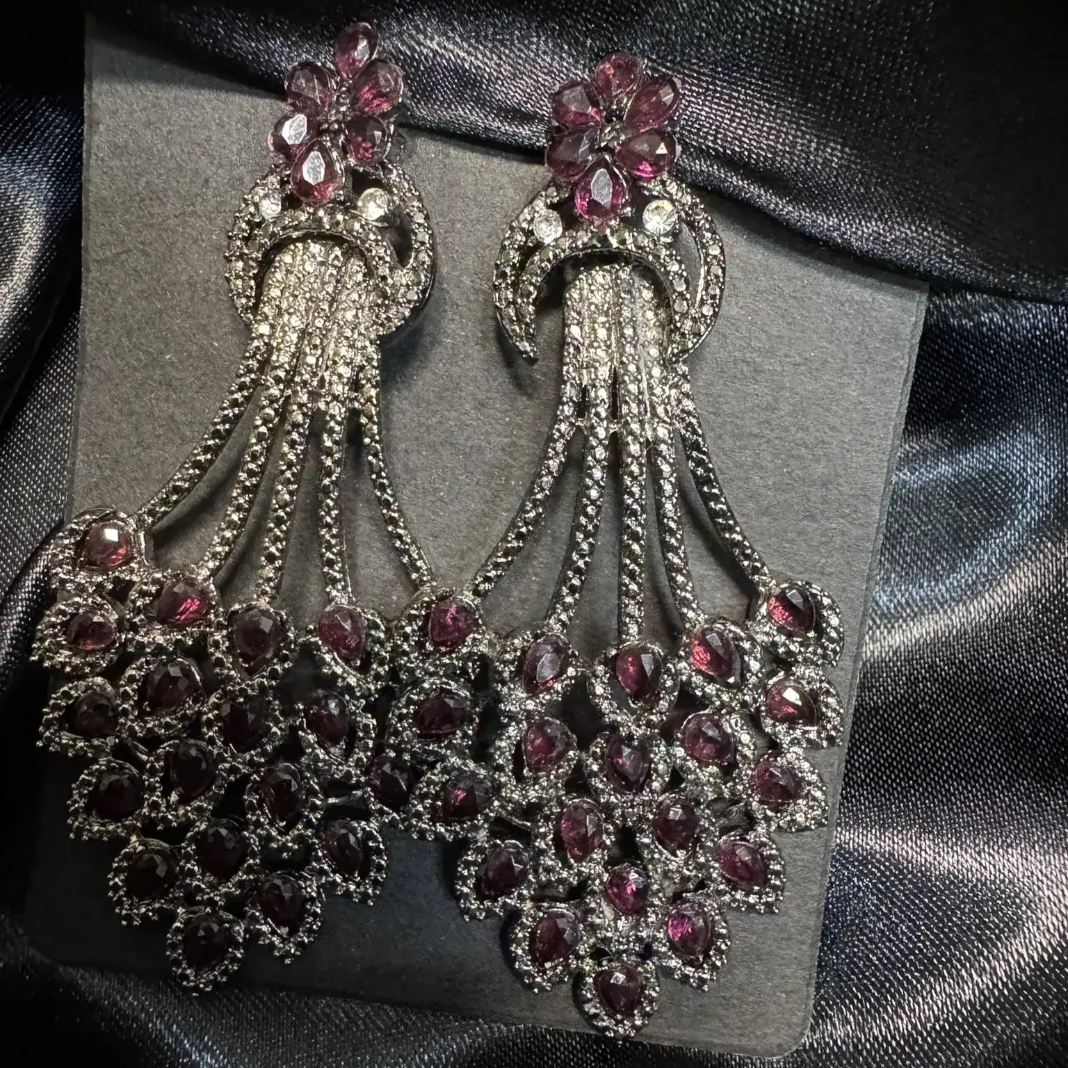 Pair of ornate earrings with hotpink gemstones on a black satin background
